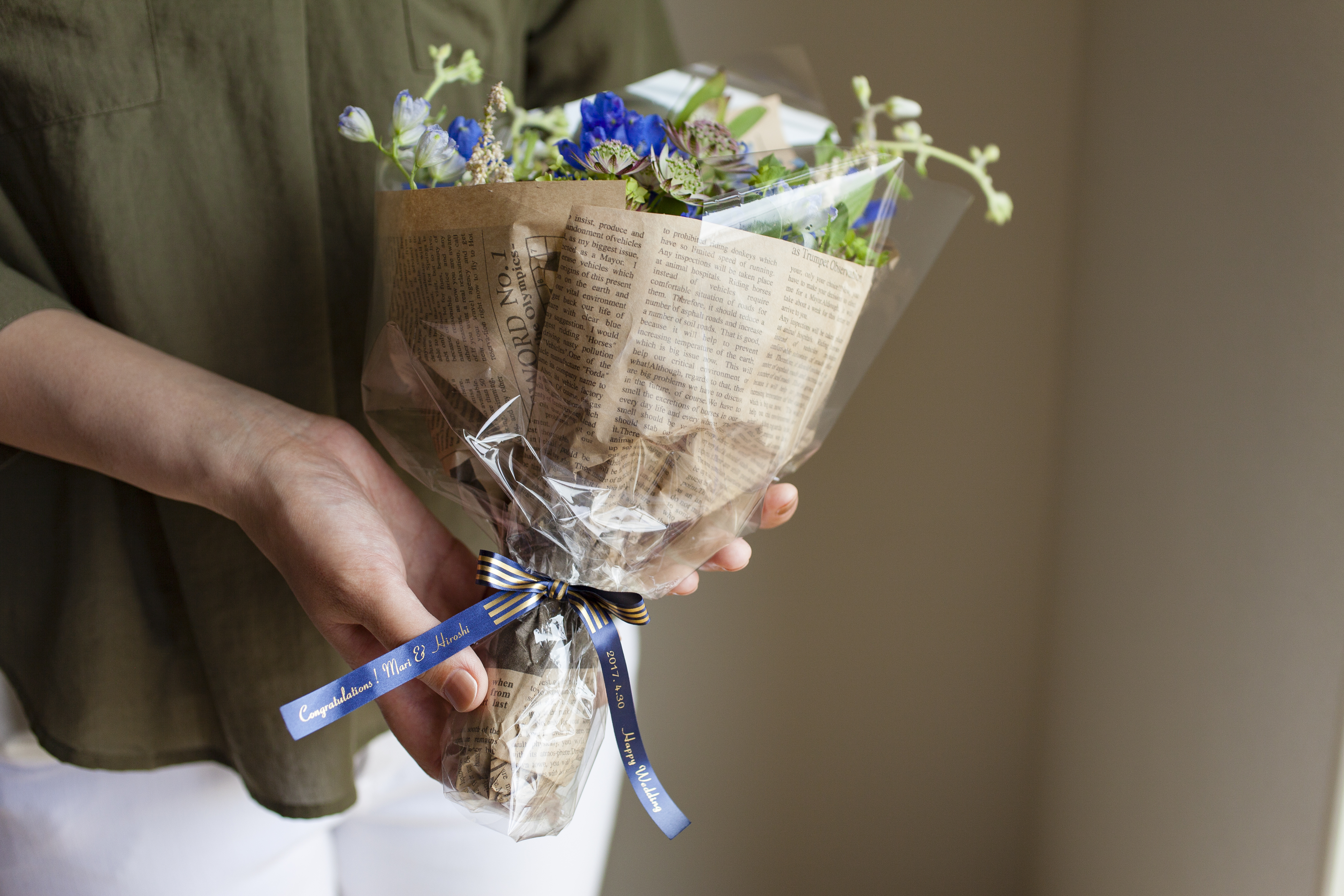 Eine Person hält einen Blumenstrauß, der in Papier eingewickelt und mit einem Band gebunden ist.