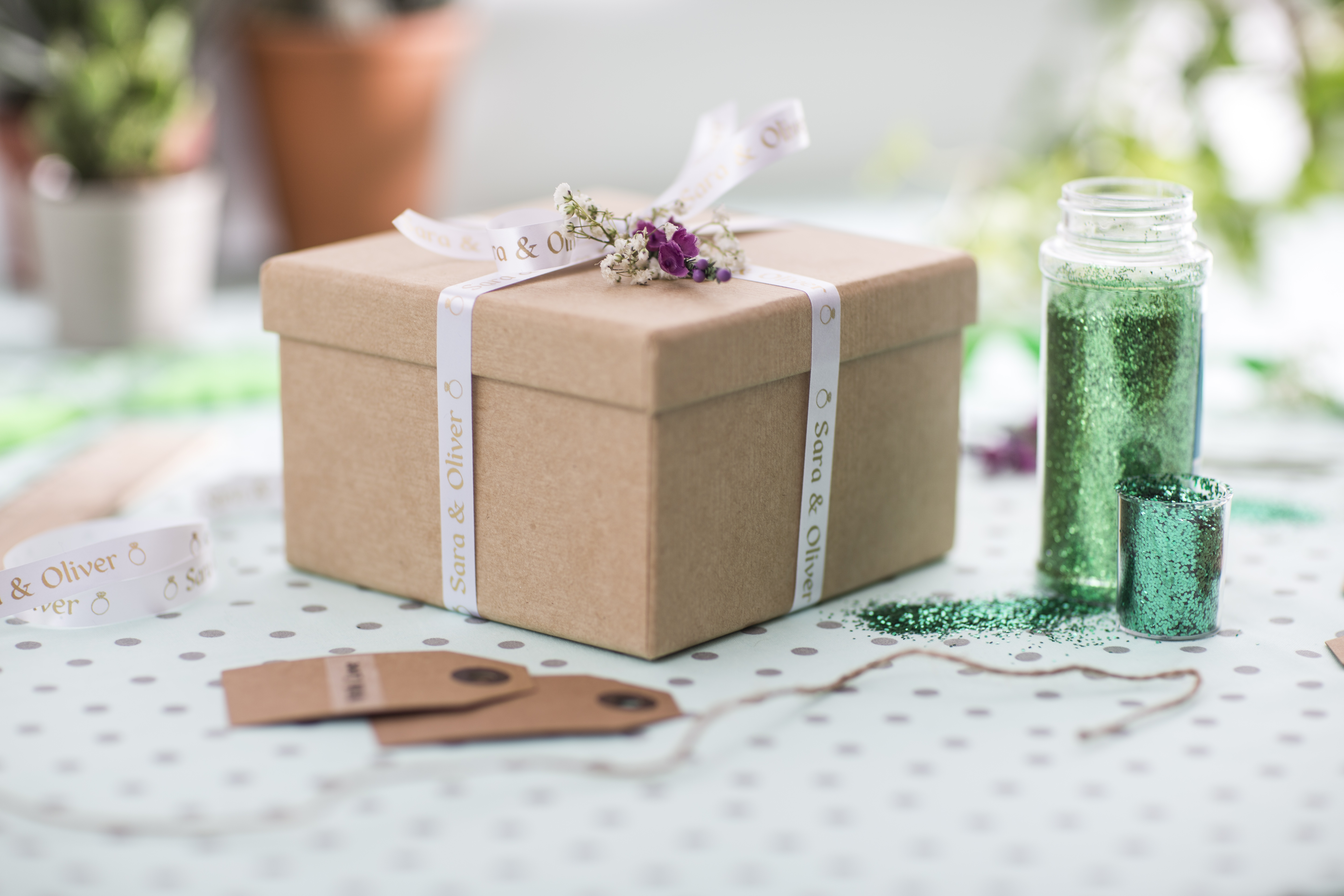 Boîte cadeau marron avec un ruban blanc et des fleurs. Paillettes et étiquettes sur une surface tachetée.