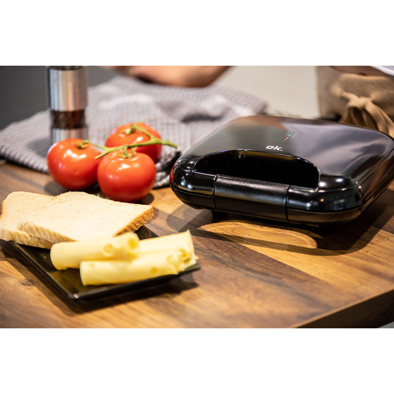 Toastiera con pane, pomodori e formaggio su tavolo di legno.
