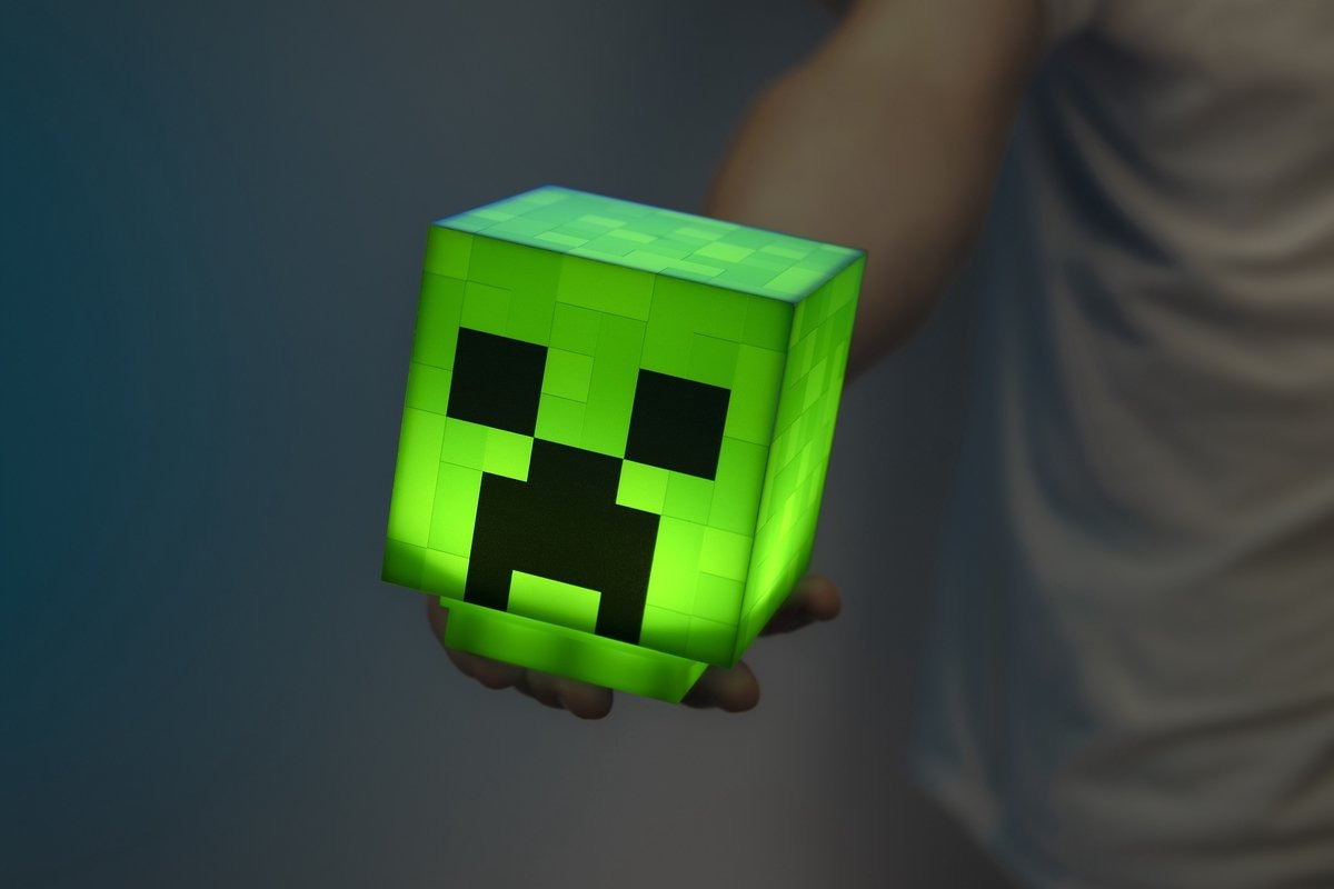 Green Minecraft Creeper head lamp, held by hand, glowing.  Dark background.