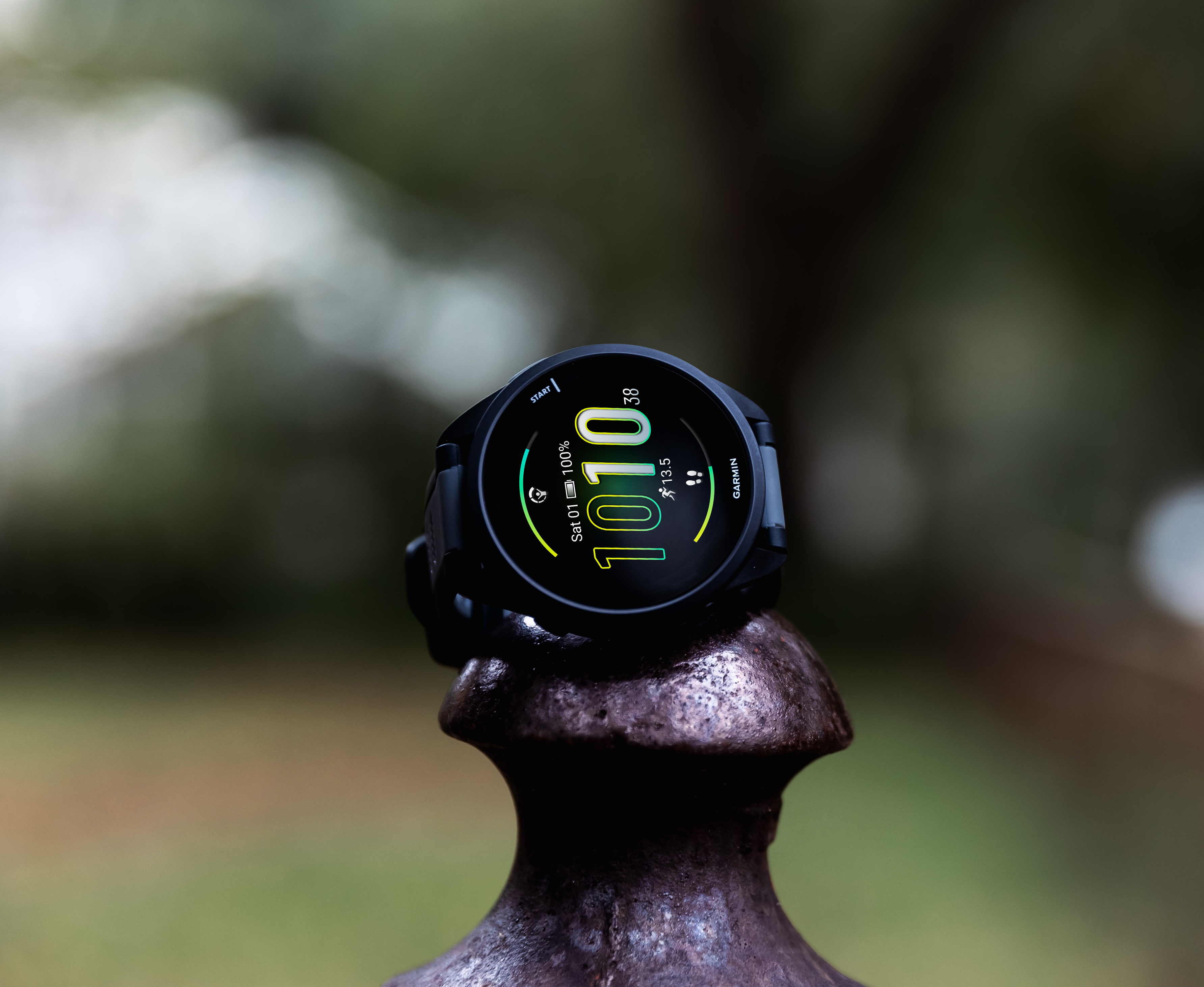 Schwarze Smartwatch auf Metallpfosten, verschwommener grüner Hintergrund.