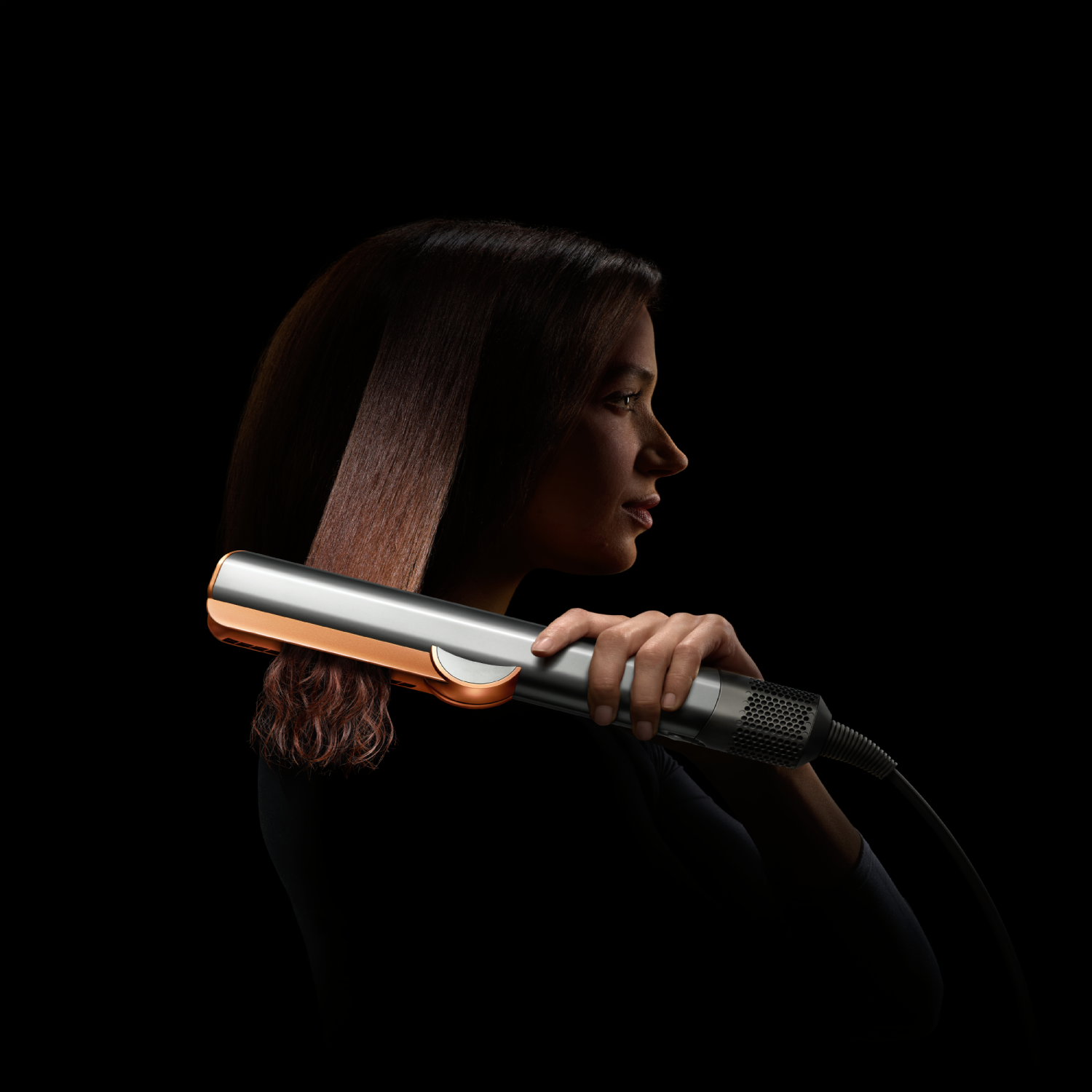 Una mujer usando una plancha para el cabello plateada y oro rosa, con su cabello alisándose.