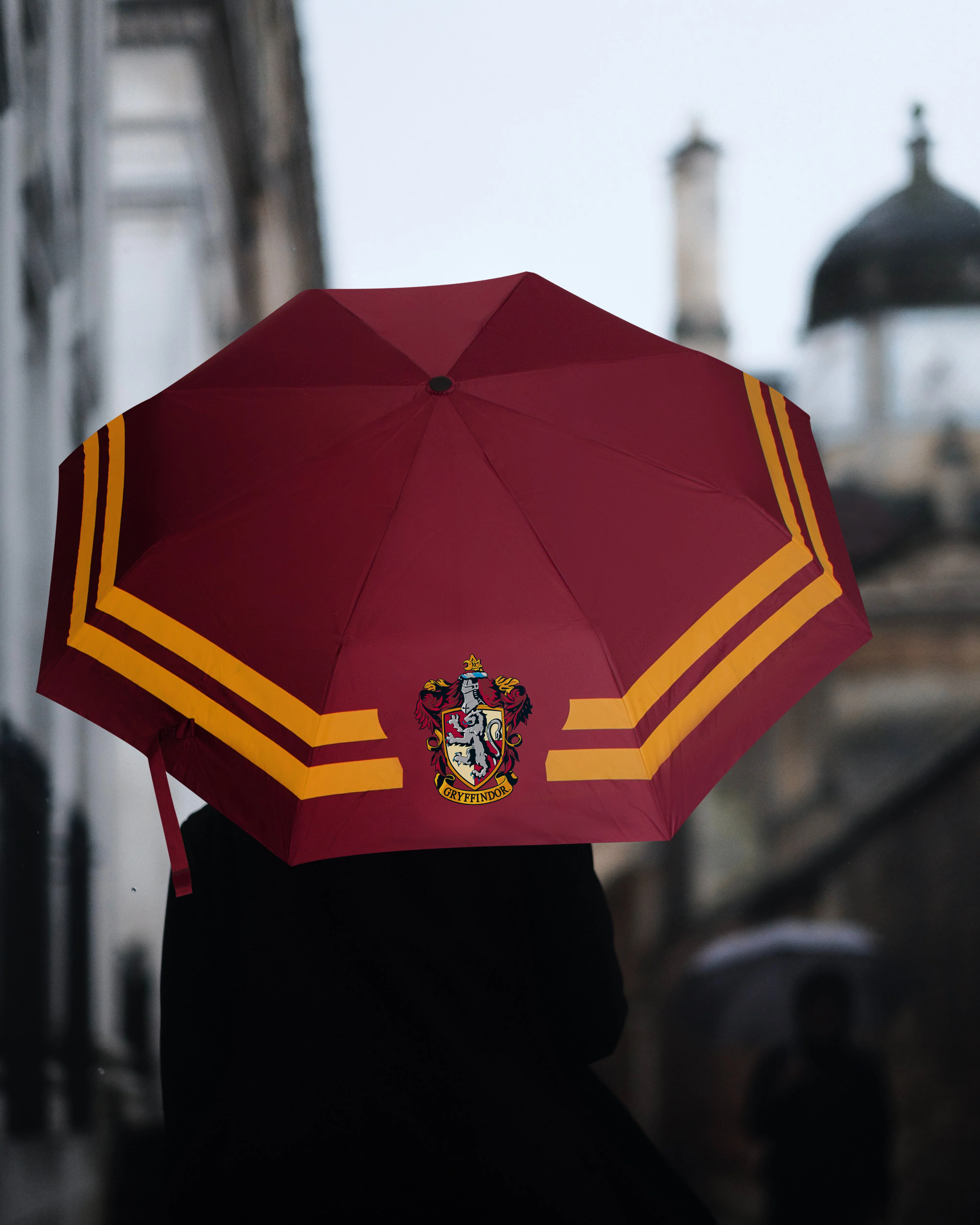 Une personne avec un parapluie bordeaux et jaune sous la pluie.