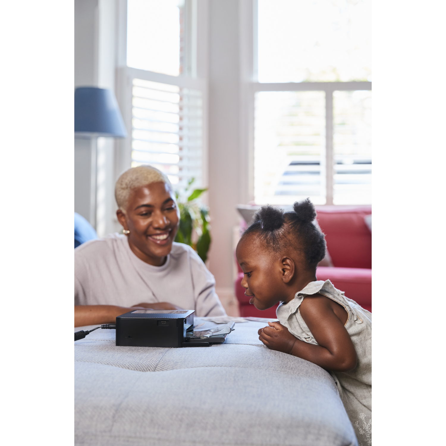 A woman and a child are looking at a device on a table. The child is smiling.