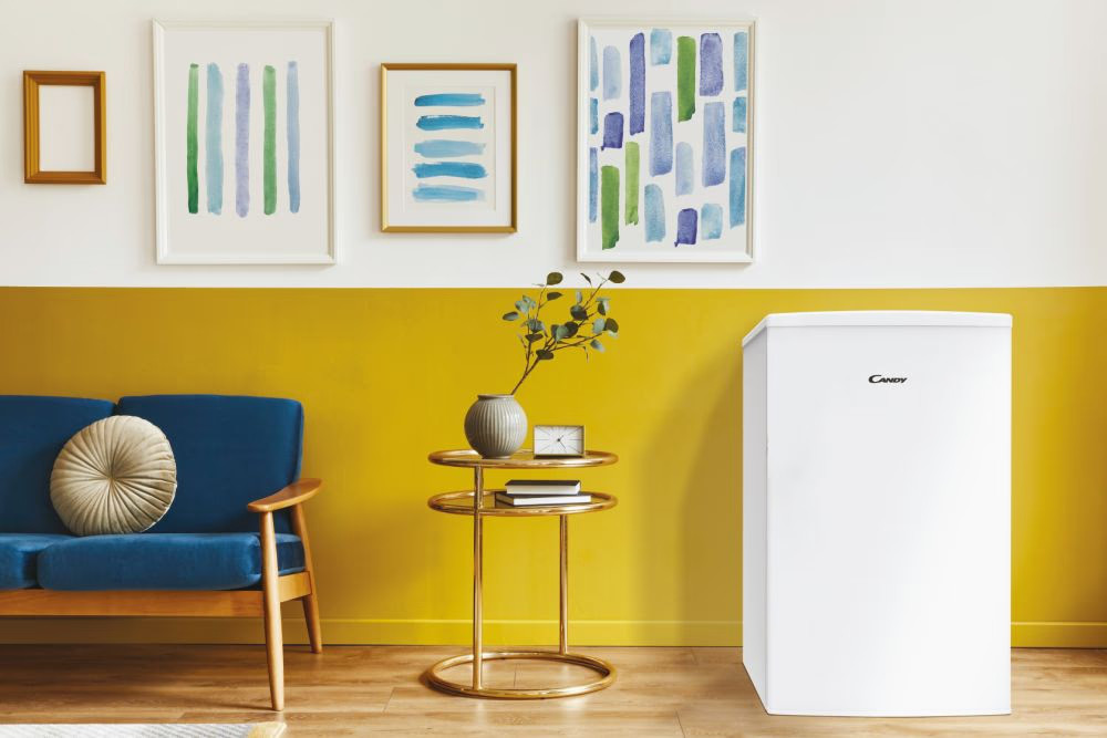 Biała lodówka Candy w pokoju. Na ścianie są obrazy i meble.