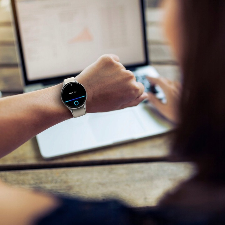 Osoba nosząca smartwatch, korzystająca z laptopa na drewnianym stole.