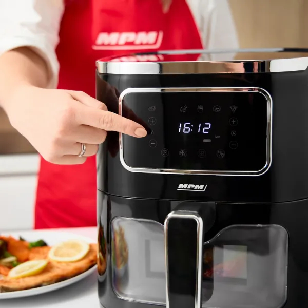 Czarna frytkownica beztłuszczowa, dłoń kobiety dotykająca wyświetlacza. Czerwony fartuch w tle.