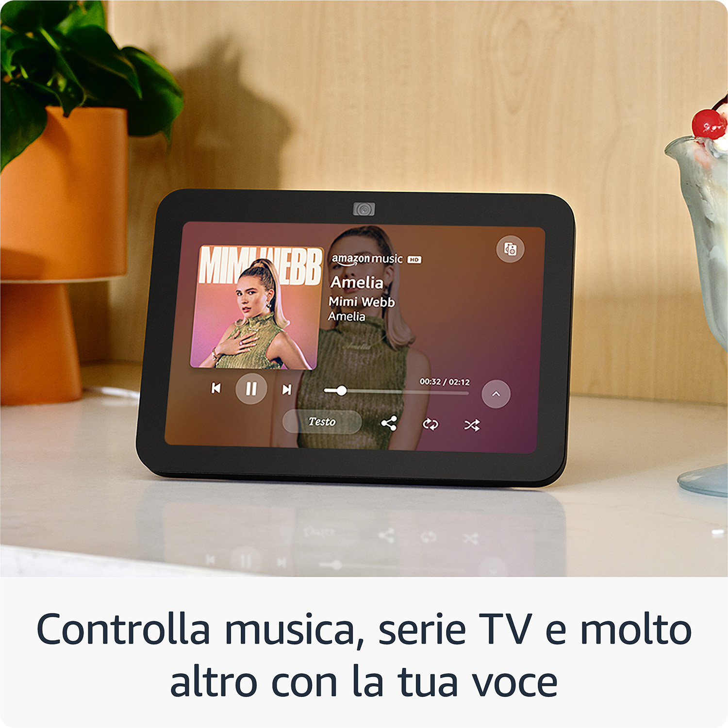 Un tablet nero mostra musica di Mimi Webb. Una pianta e una coppa gelato sul tavolo.