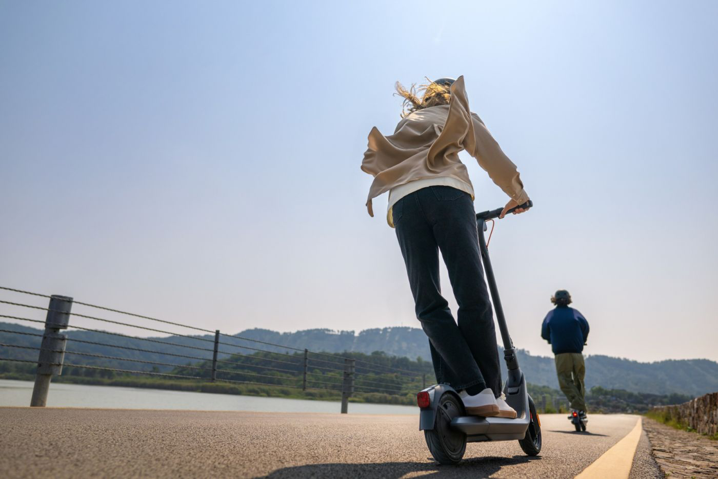 Nő elektromos robogón, második személy a háttérben.