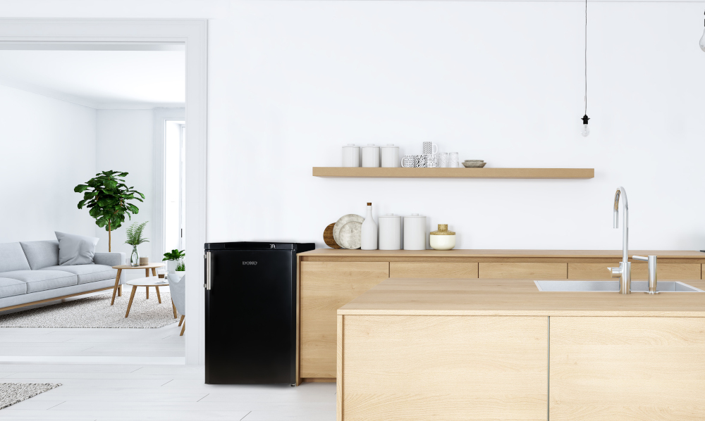Un réfrigérateur noir à côté d'un comptoir en bois dans une cuisine moderne. Salon en arrière-plan.