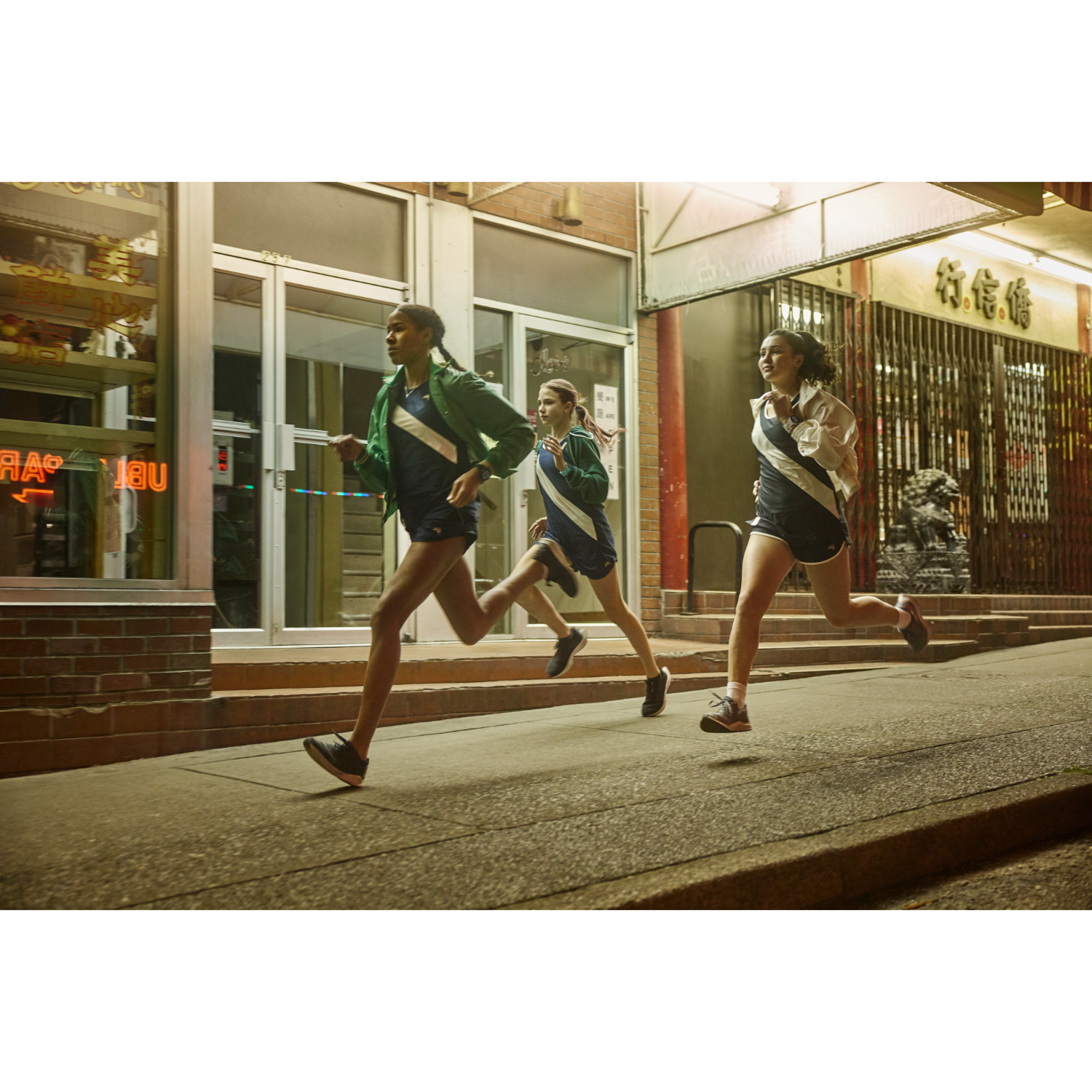 Drie jonge vrouwen rennen 's nachts op een straat in de stad, verlicht.