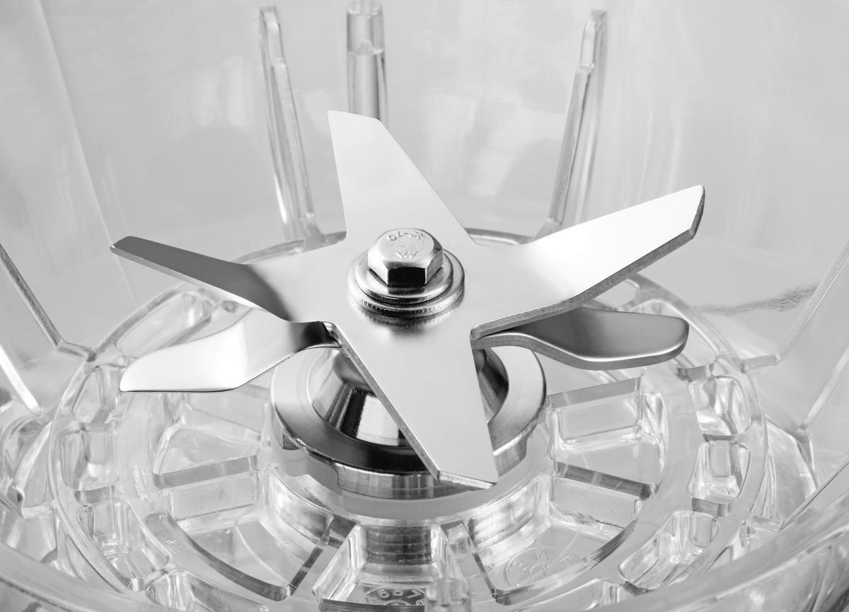 Nahaufnahme einer Mixer-Klingenanordnung. Die Klingen sind glänzendes Metall, mit einer zentralen Schraube. Der Mixer-Körper ist klarer Kunststoff.