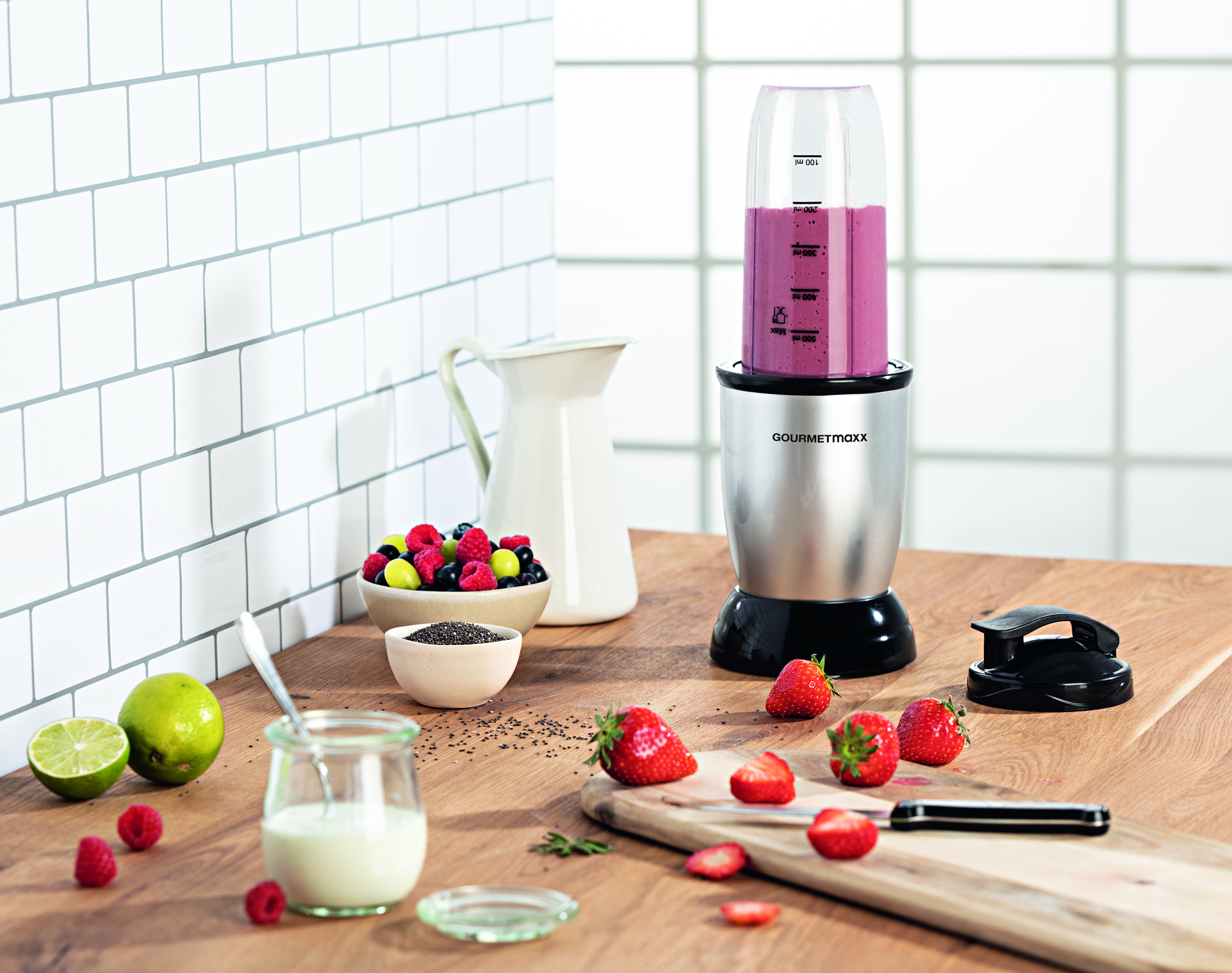 Ein Mixer mit einem rosa Smoothie, Erdbeeren und Zutaten steht auf einem Holztisch.