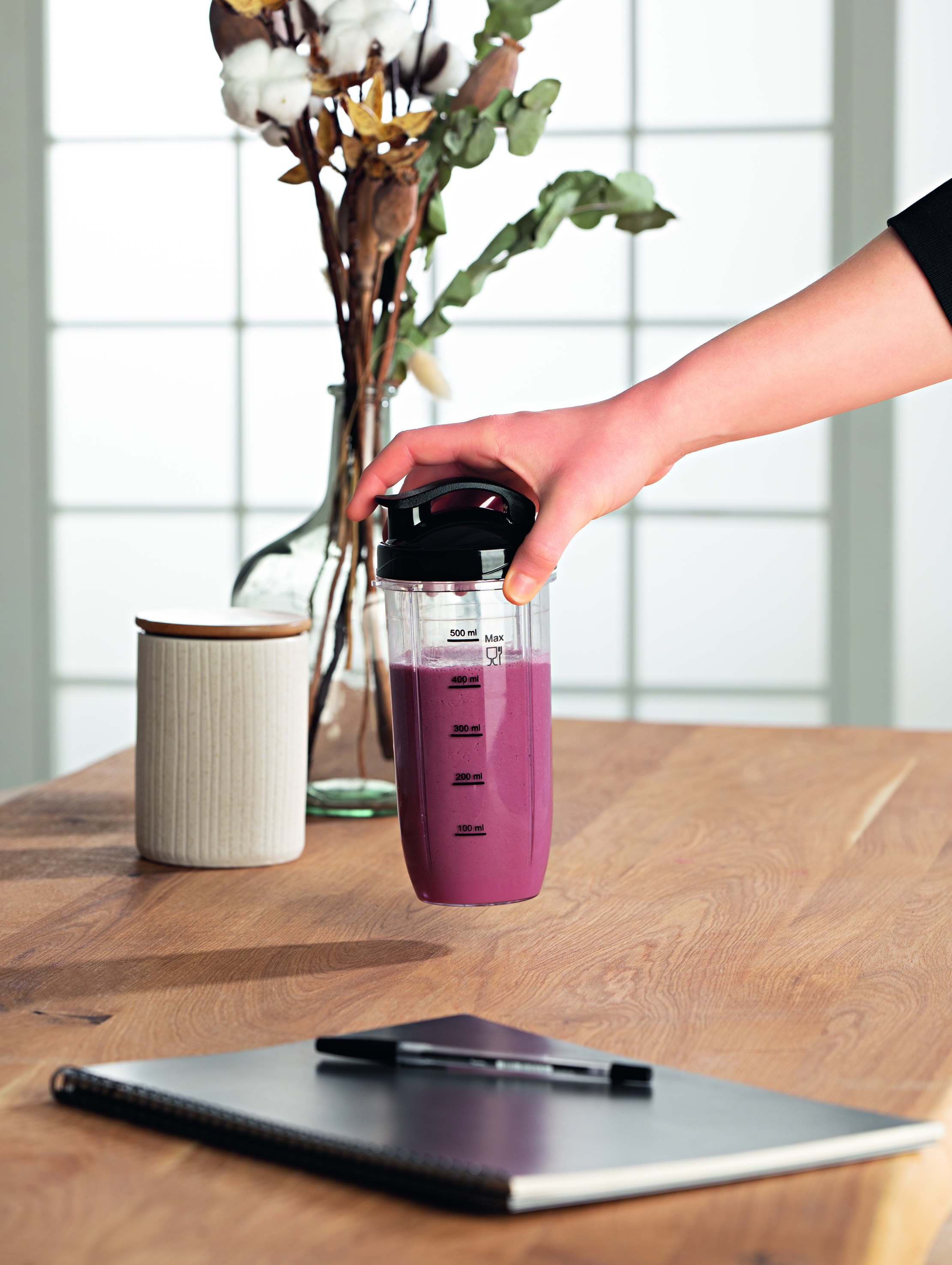 Eine Person, die eine Mixbecher mit einem lila Smoothie hält.
