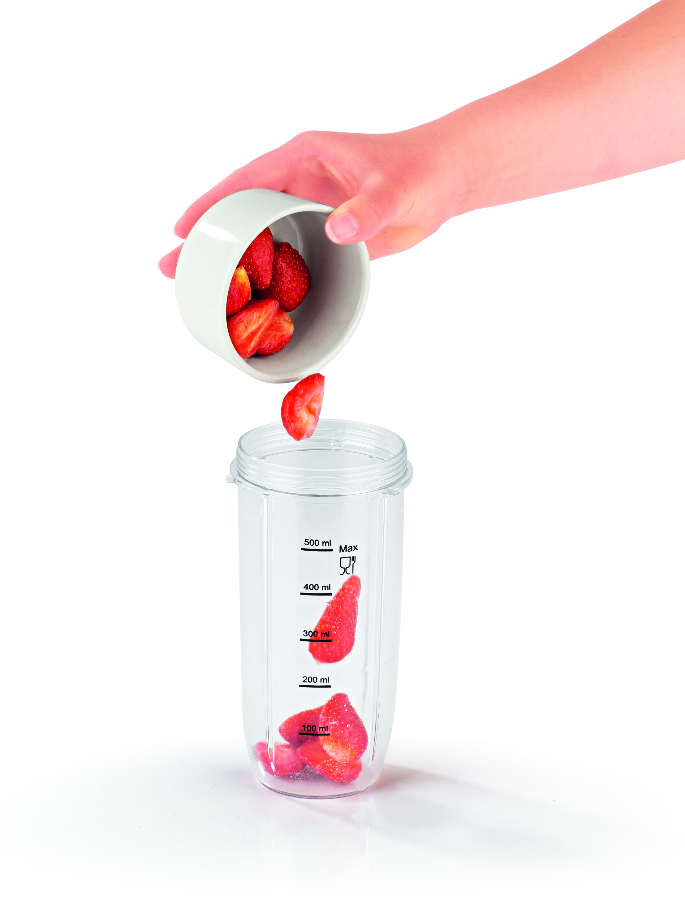 Eine Hand gießt geschnittene Erdbeeren in einen transparenten Behälter. Erdbeeren sind bereits im Behälter.