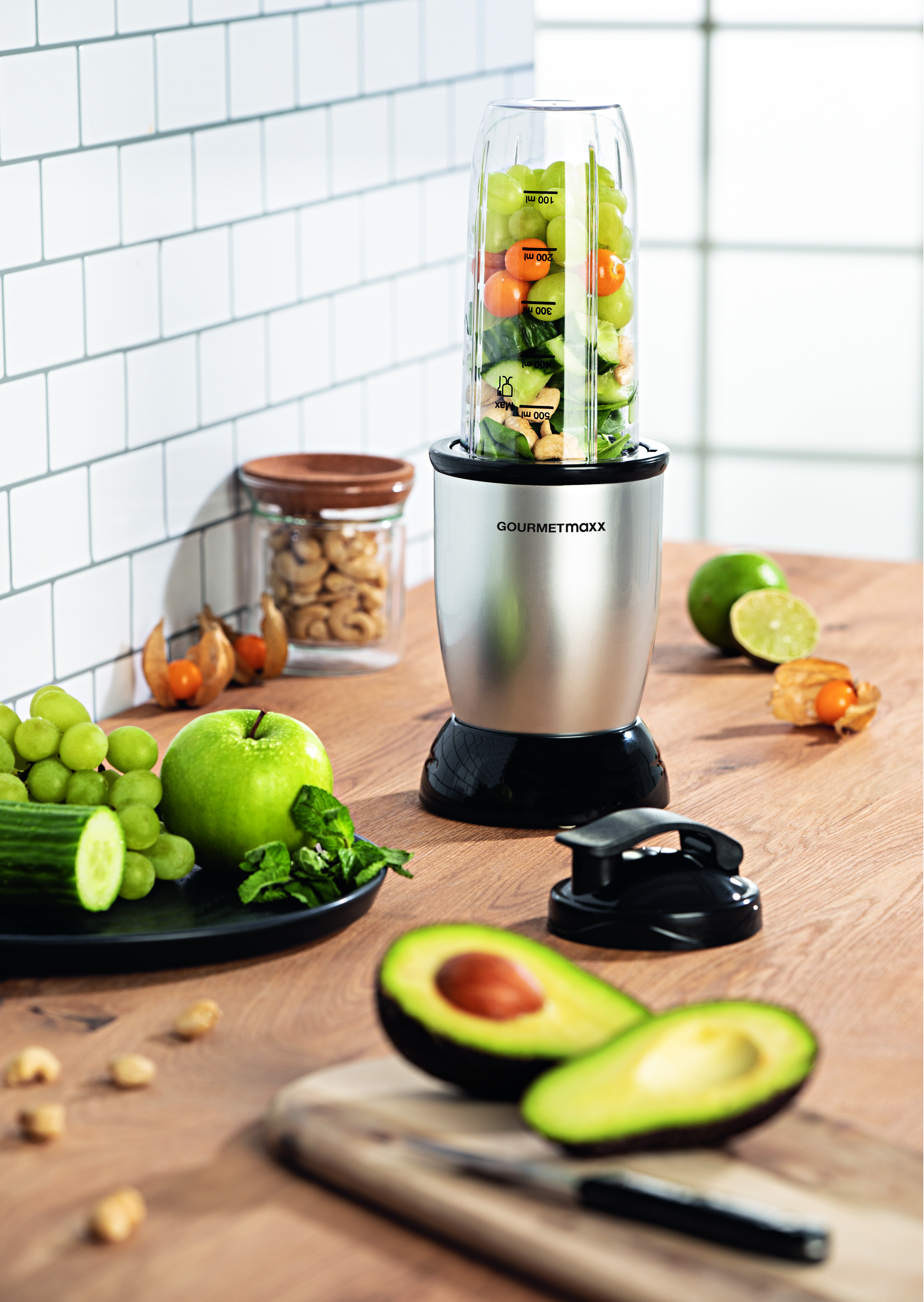 Mixer mit Früchten und Gemüse. Avocado, Früchte und eine Limette auf dem Tisch.