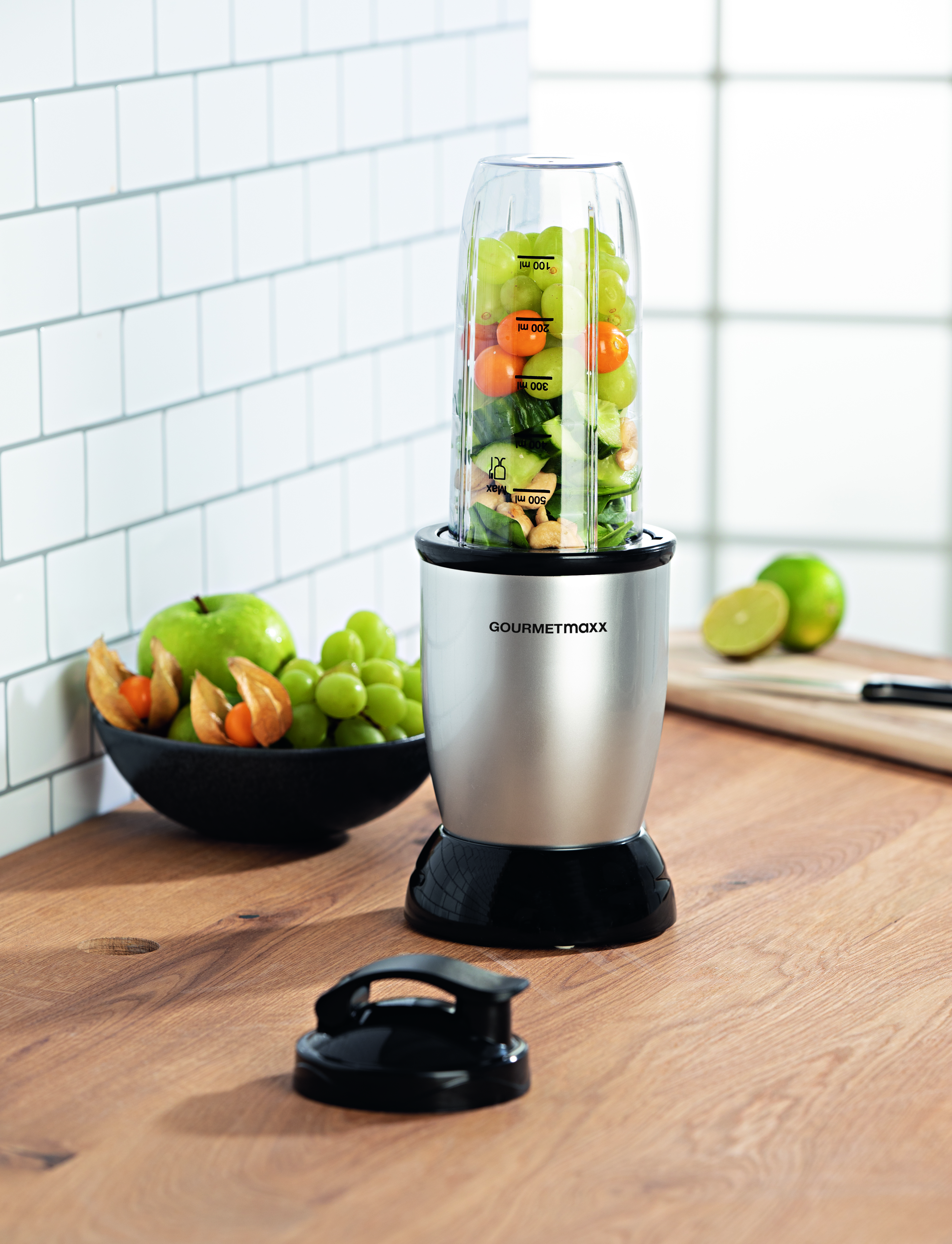 Ein Mixer mit Früchten darin. Es gibt einen grünen Apfel und eine Schüssel mit Früchten.