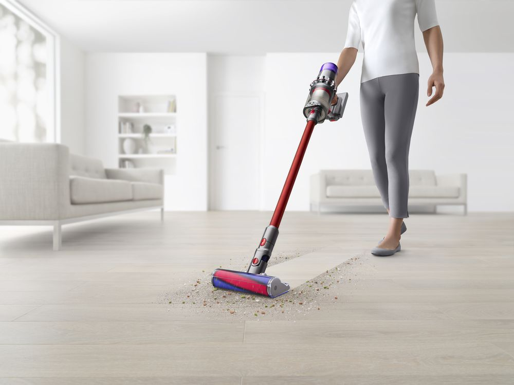 Eine Person saugt einen Holzboden. Der Staubsauger ist rot und silber. Der Raum ist weiß.