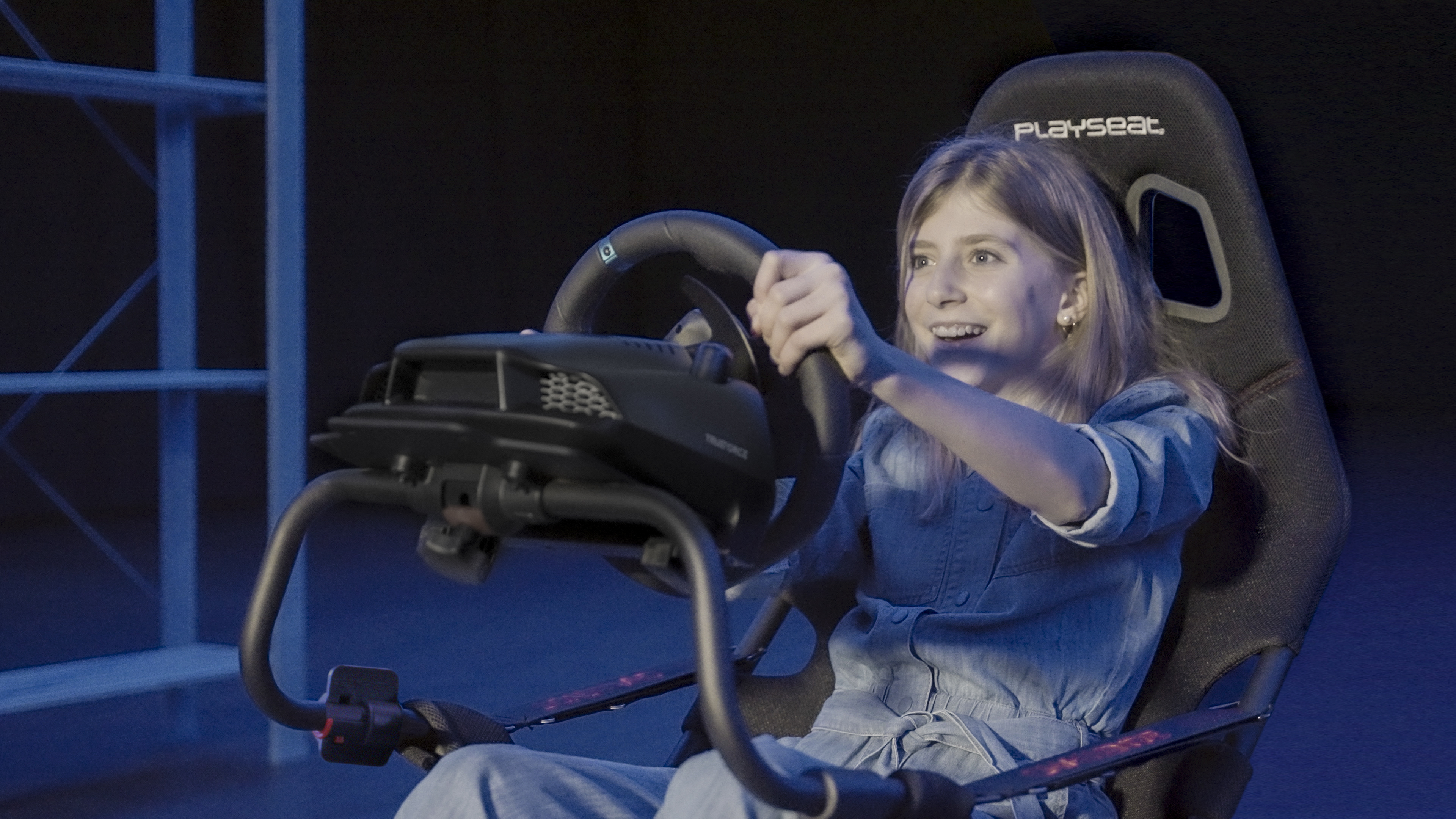 Girl in racing seat playing driving simulator. Steering wheel in hands.