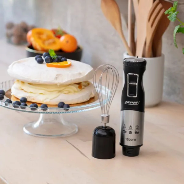 Ciasto z borówkami i plasterkiem pomarańczy, trzepaczka i mikser ręczny na stole.