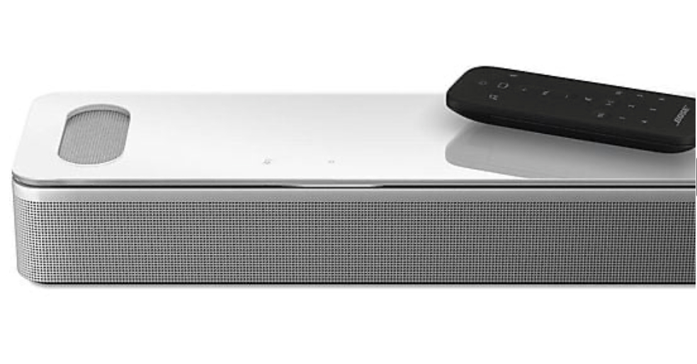 Eine weiße Soundbar mit einer Fernbedienung oben. Sie hat ein silbernes Mesh.
