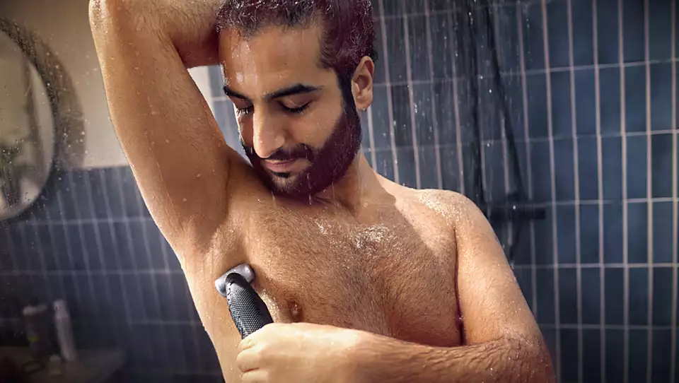 Egy férfi a zuhany alatt, Philips body groomerrel borotválja a hónalját.