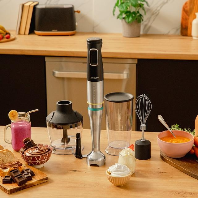 Una escena de cocina con una licuadora, batido, chocolate y otros alimentos sobre una mesa de madera. Una tostadora y una planta están en el fondo.