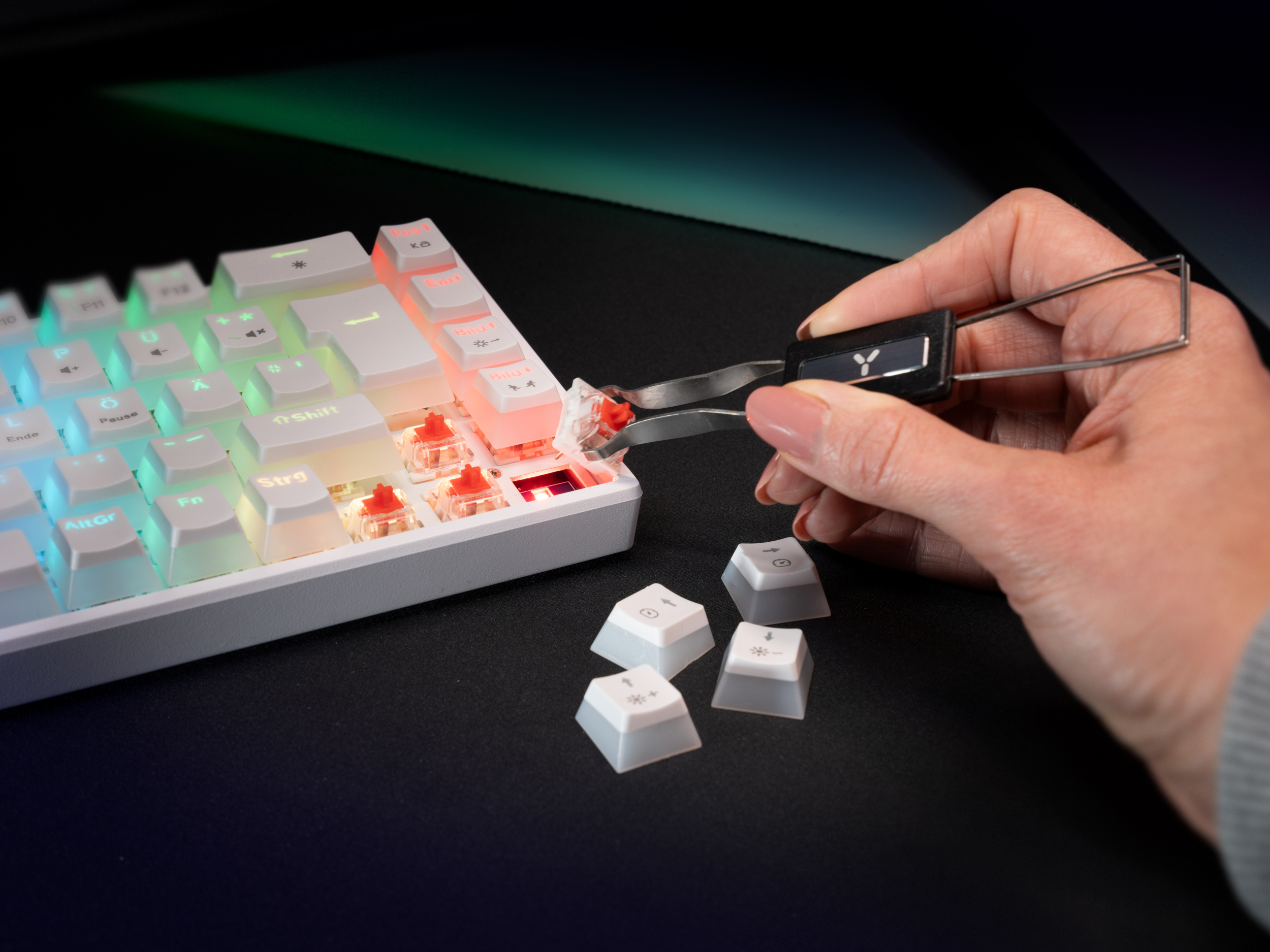 Eine Hand, die einen Keycap-Abzieher hält, um eine Tastenkappe von einer weißen mechanischen Tastatur zu entfernen.