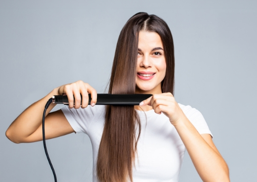Kobieta z prostymi brązowymi włosami używająca prostownicy.
