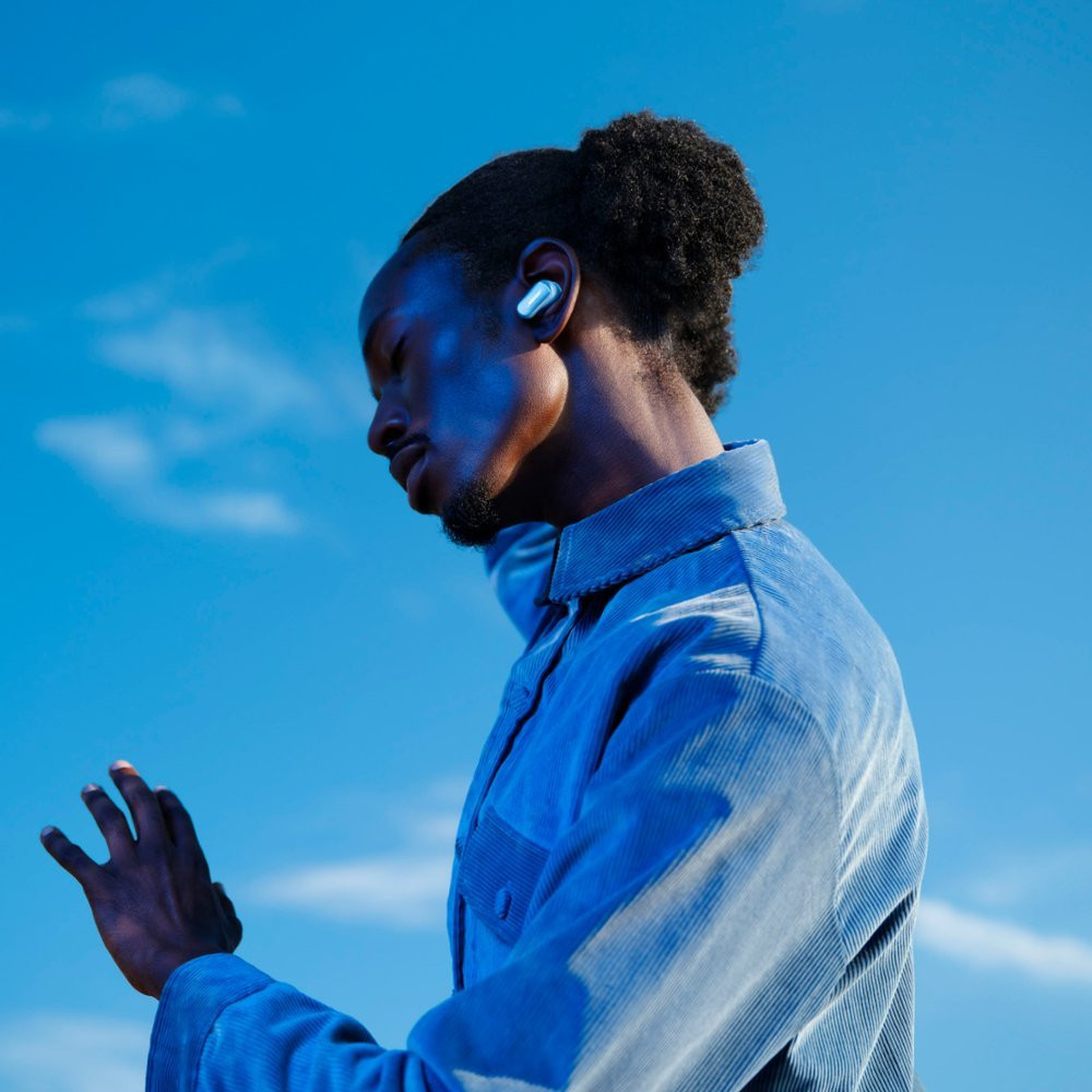 A man with blue light on his face, wearing a blue shirt, and one earbud in his ear.