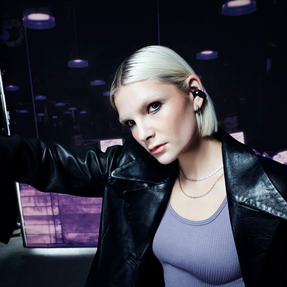 Woman with short blonde hair, wearing a leather jacket.