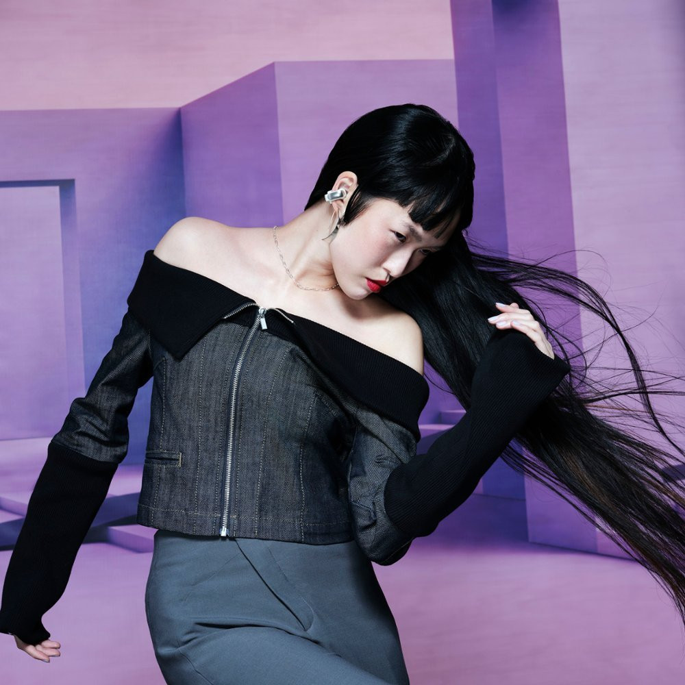Woman with long black hair, wearing off-shoulder black top, silver earrings, and red lipstick.