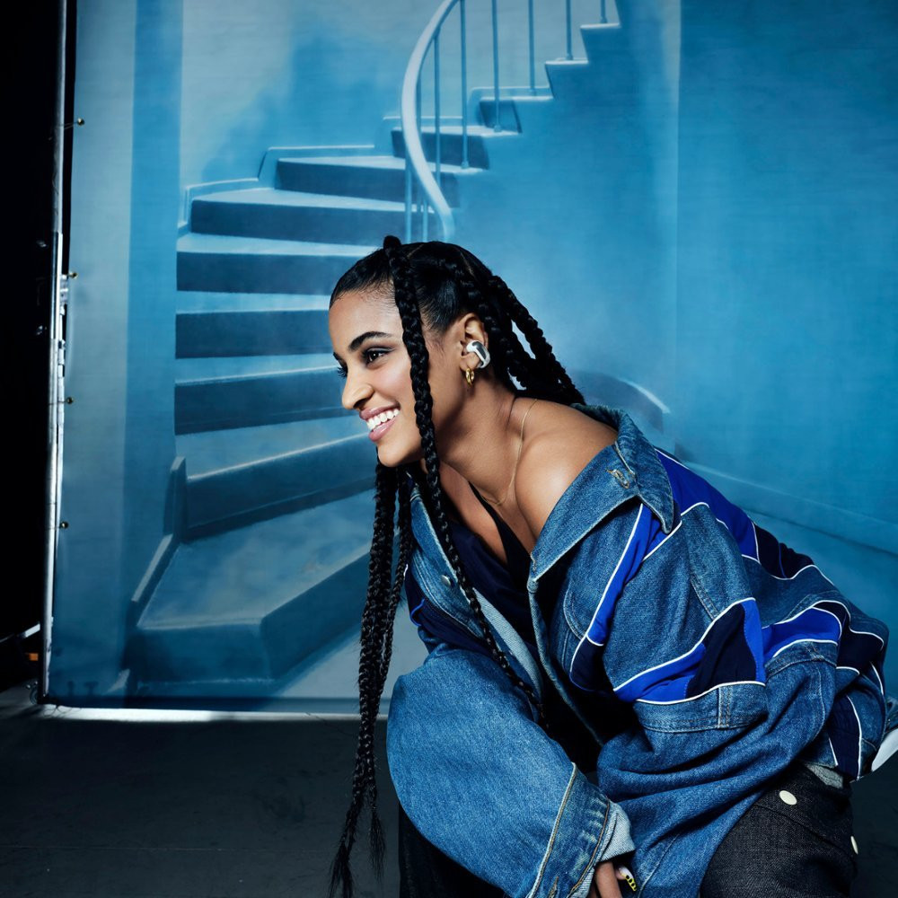 Woman with long braids, denim jacket, and ear accessories.
