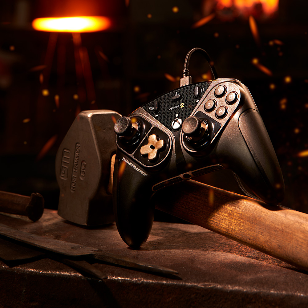 Schwarzer Gamecontroller. Hammer und Metalloberfläche. Funken und Feuer drumherum.