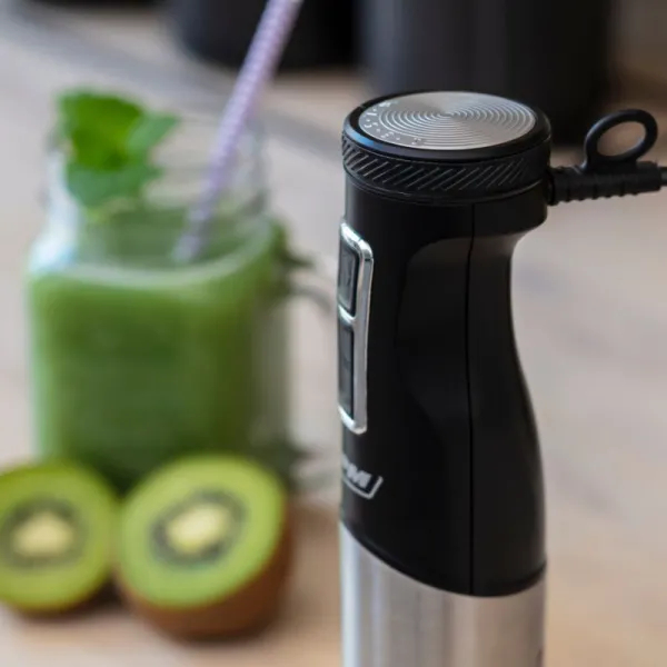 Zbliżenie czarnego blendera ręcznego ze srebrną podstawą, kiwi i koktajlem w tle.