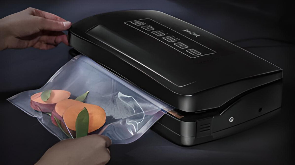 Czarna zgrzewarka próżniowa zamykająca worek z plasterkami pomarańczy i zielonymi liśćmi.