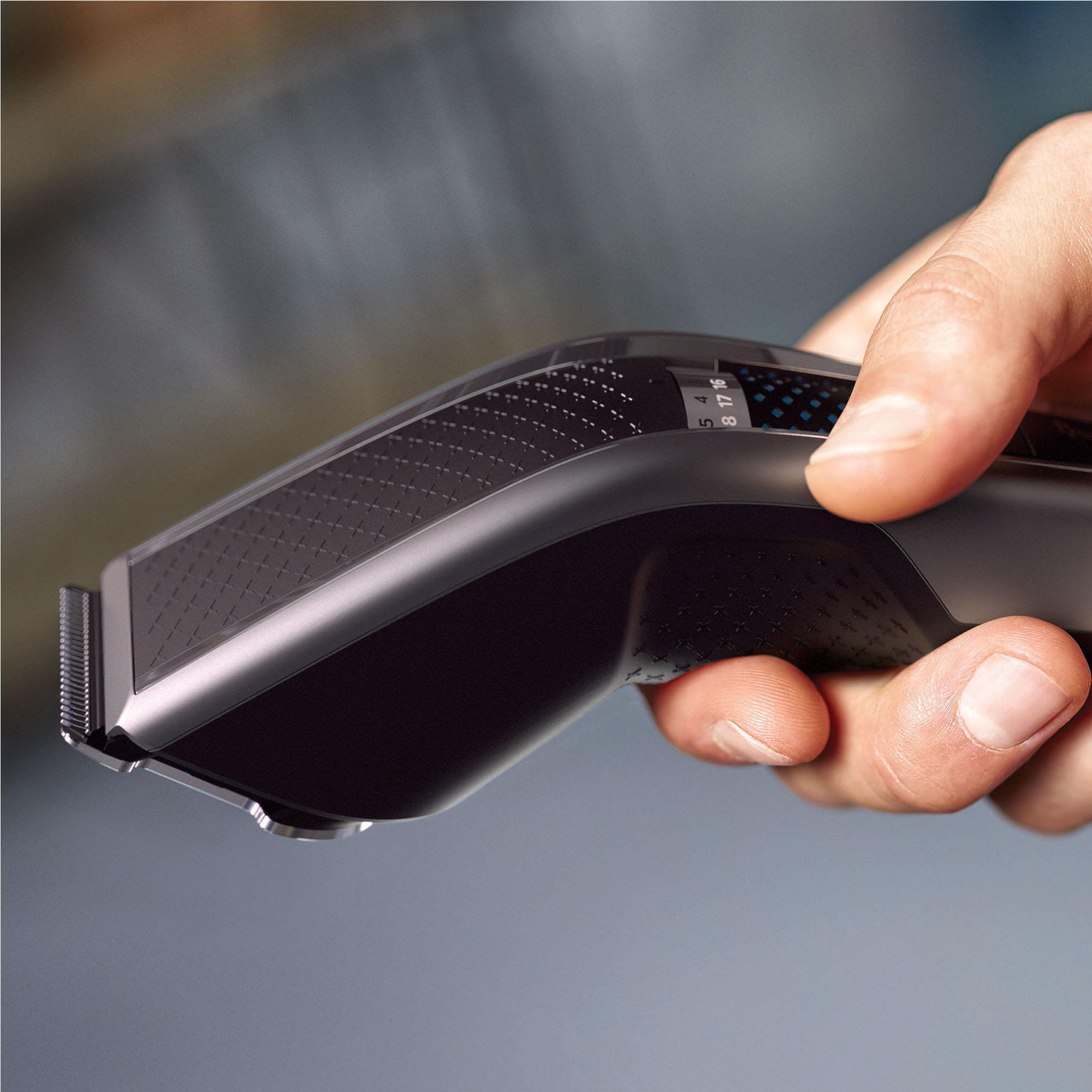 Dłoń trzymająca czarno-szarą maszynkę do włosów, ujęcie z bliska.