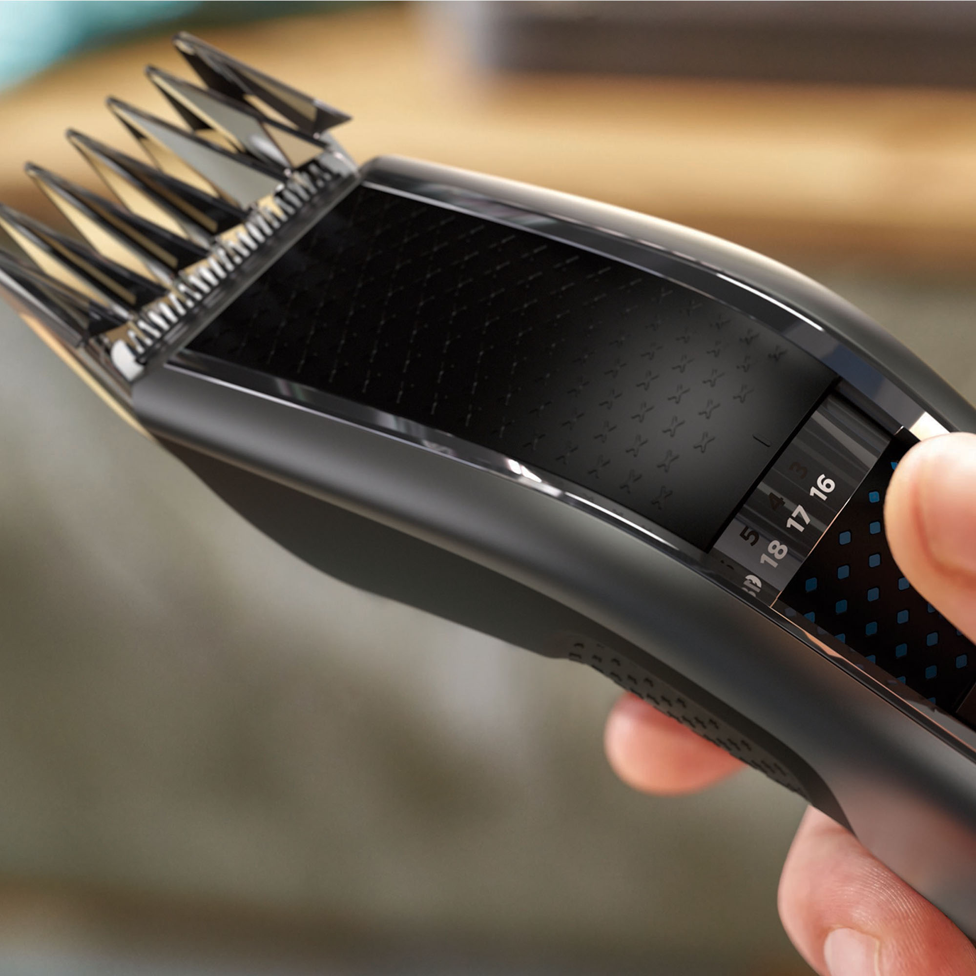 Czarna maszynka do włosów z widocznymi ustawieniami. Dłoń reguluje długość ostrza. Tło jest rozmyte.