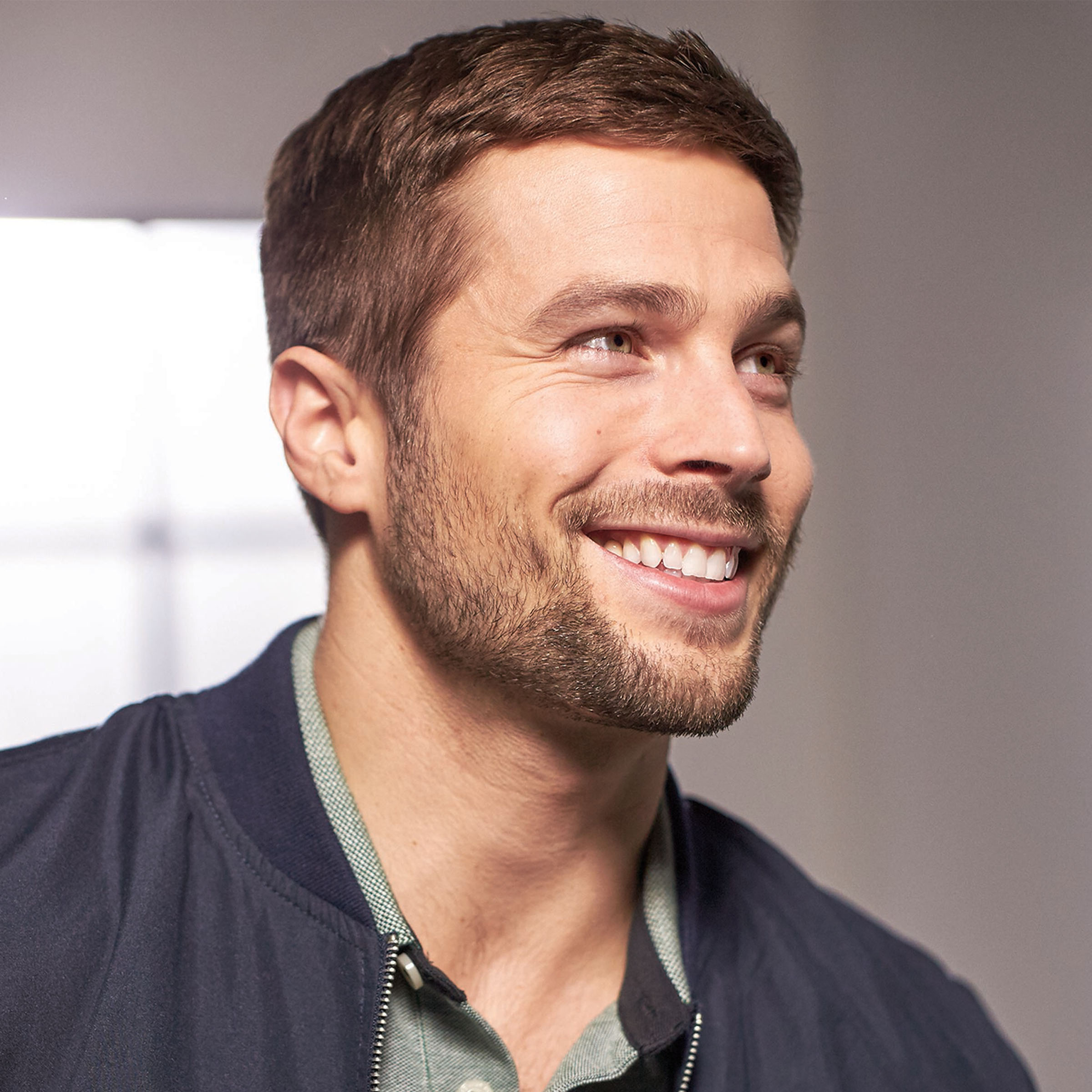 Uśmiechnięty mężczyzna z brązowymi włosami patrzący w bok, w kurtce.