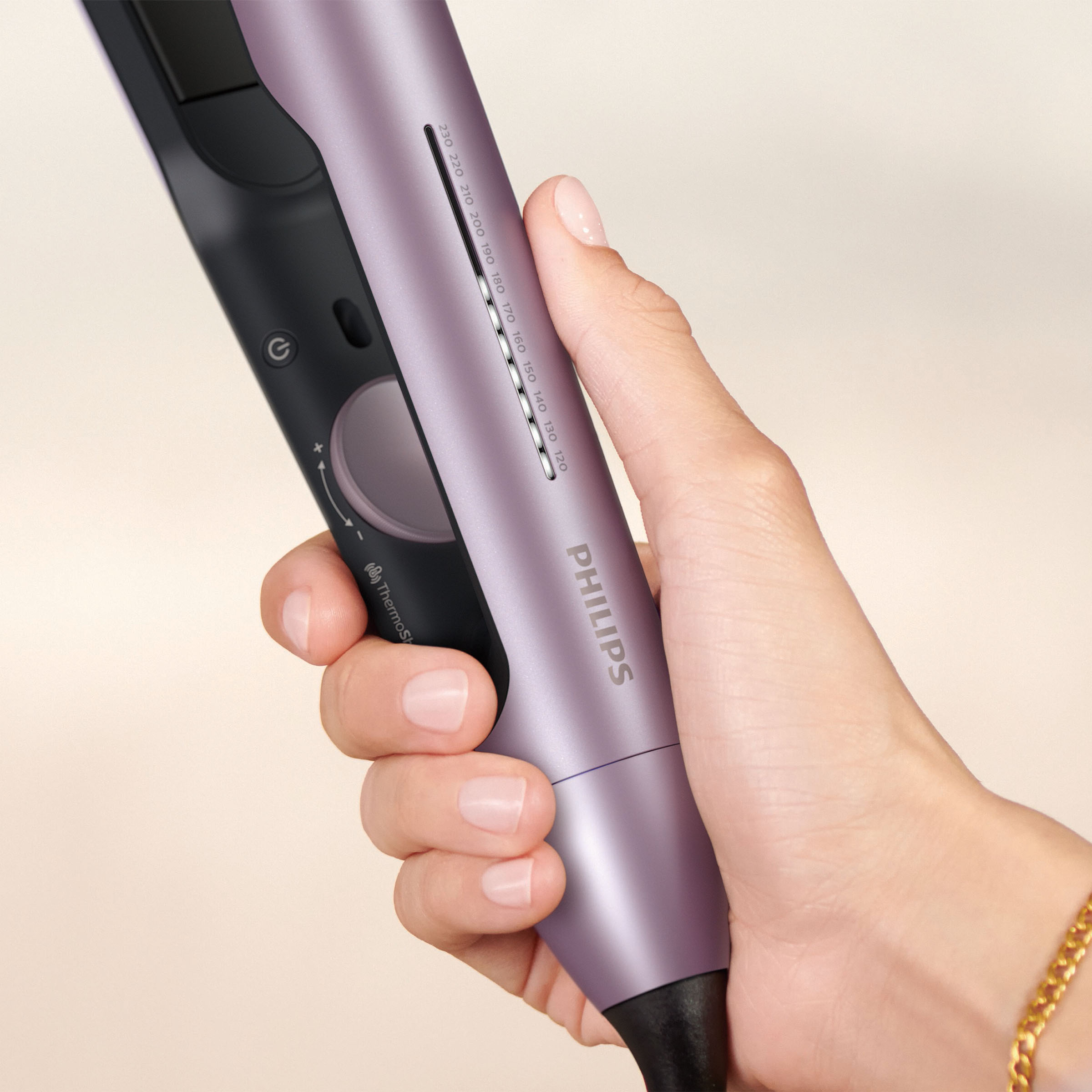 Dłoń kobiety trzymająca fioletową prostownicę z ustawieniami temperatury.