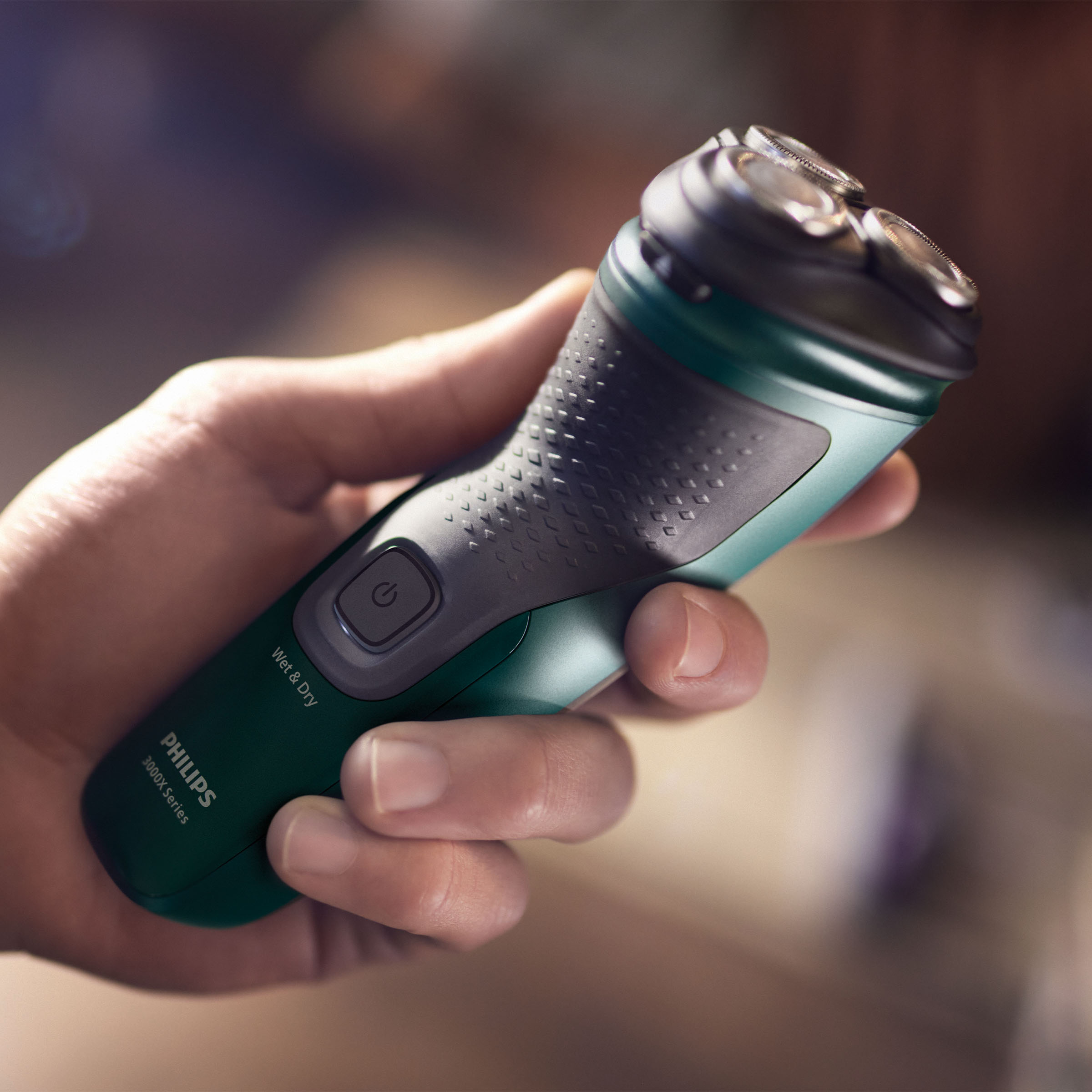 Dłoń trzymająca zielono-szarą golarkę elektryczną.