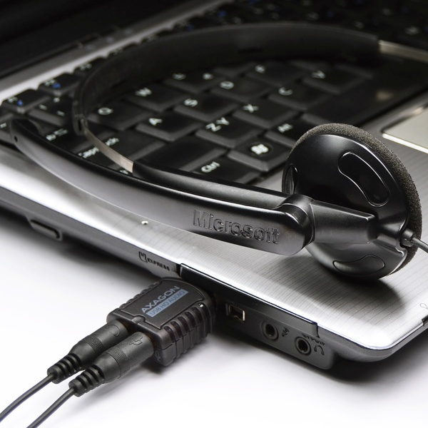 Fekete Microsoft fejhallgató és egy fekete audio adapter egy laptopon.