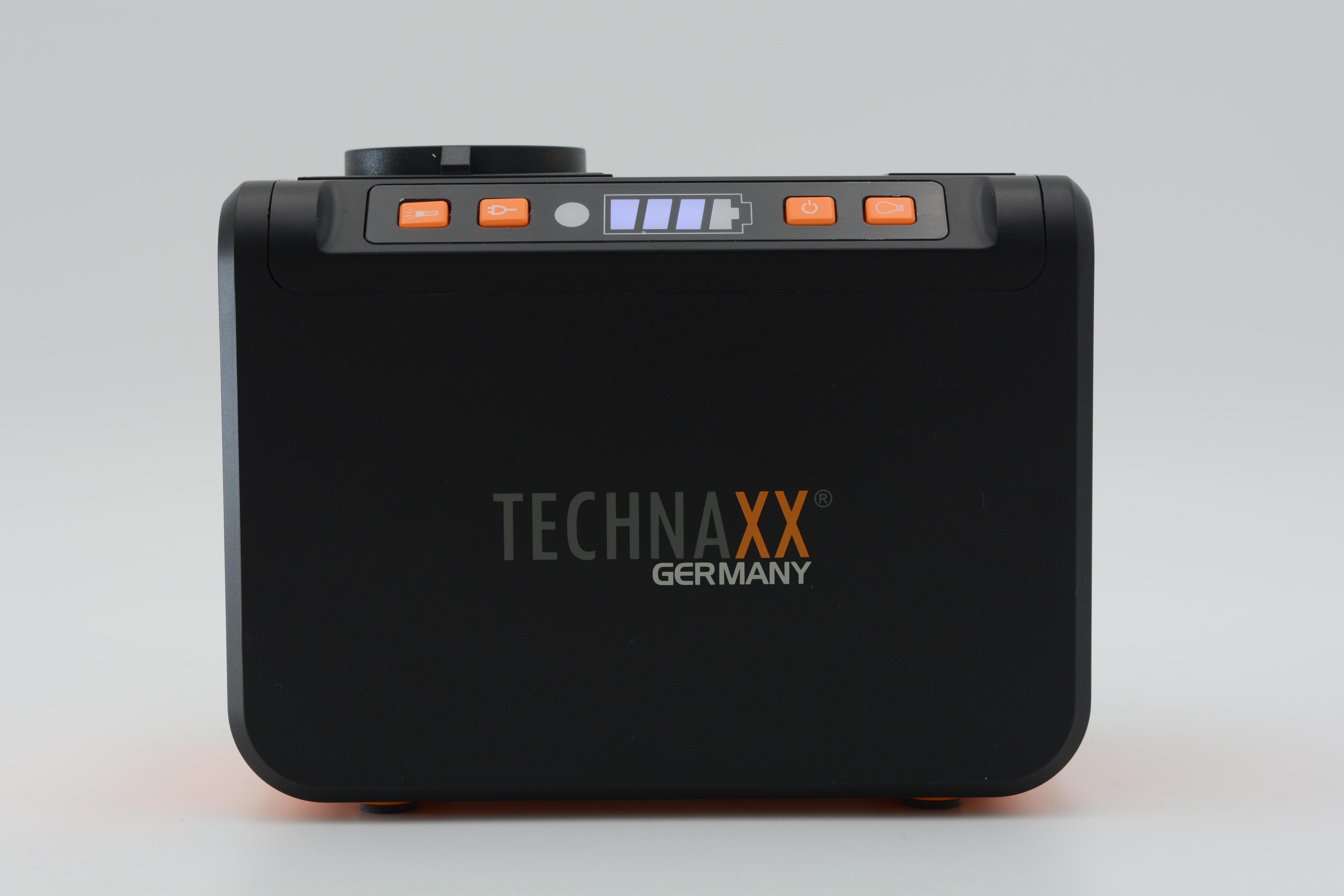Eine schwarze Powerstation mit orangefarbenen Knöpfen, mit Akkuladestand und 'TECHNAXX GERMANY'.