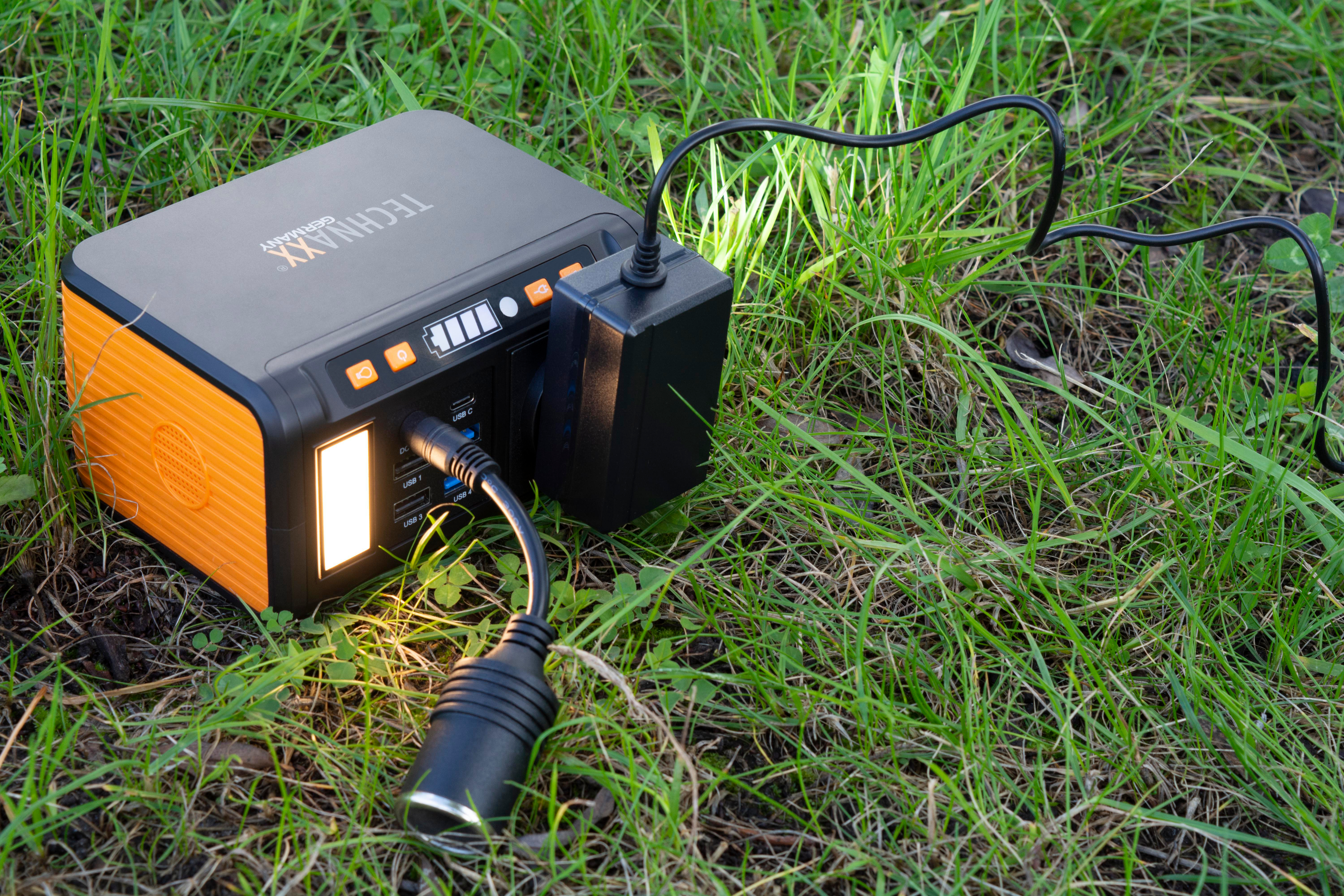 Ein orangefarbenes und schwarzes Kraftwerk mit einem Ladekabel im Gras.