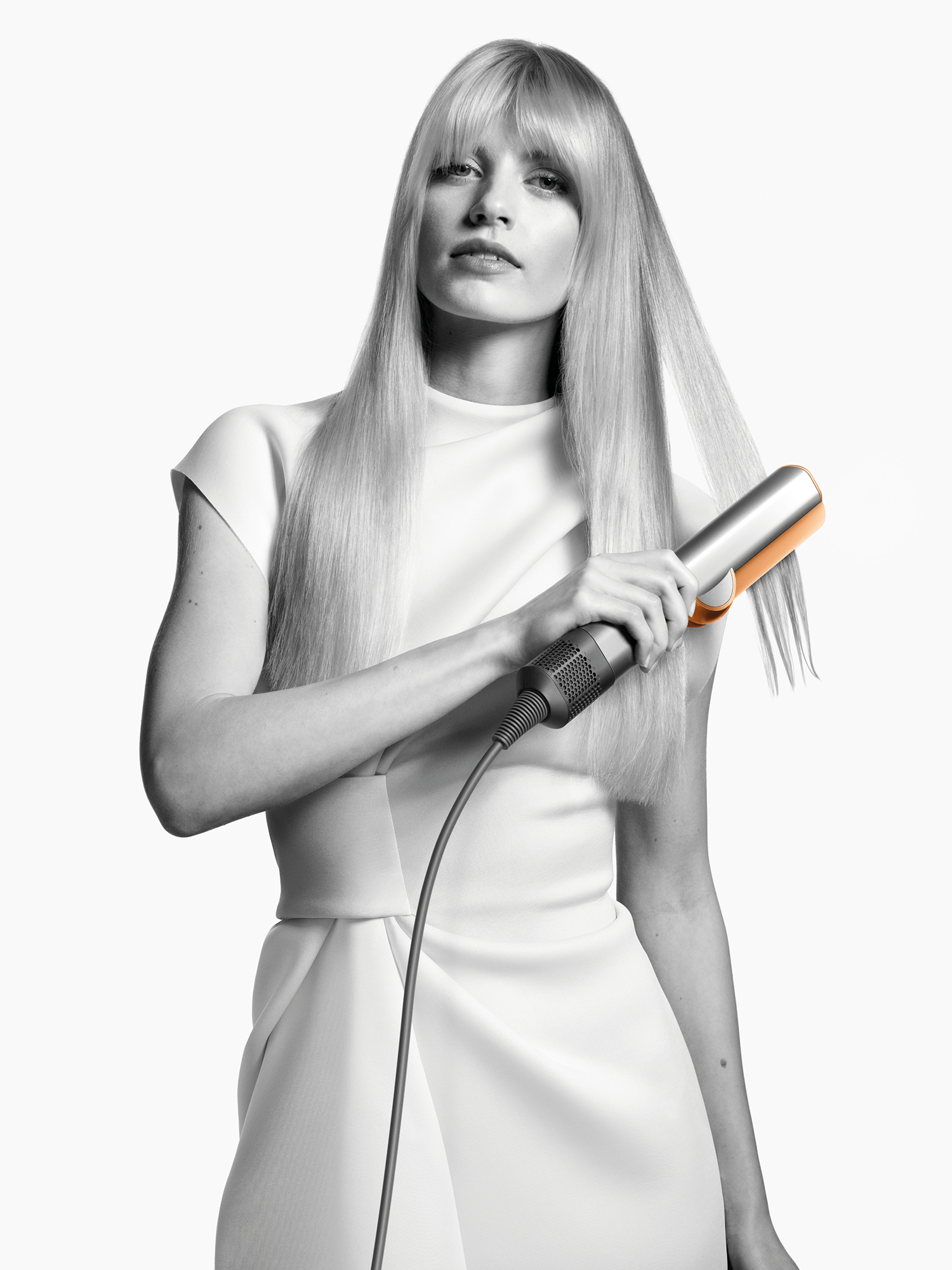 Eine Frau hält ein Glätteisen in ihrem langen, blonden Haar.