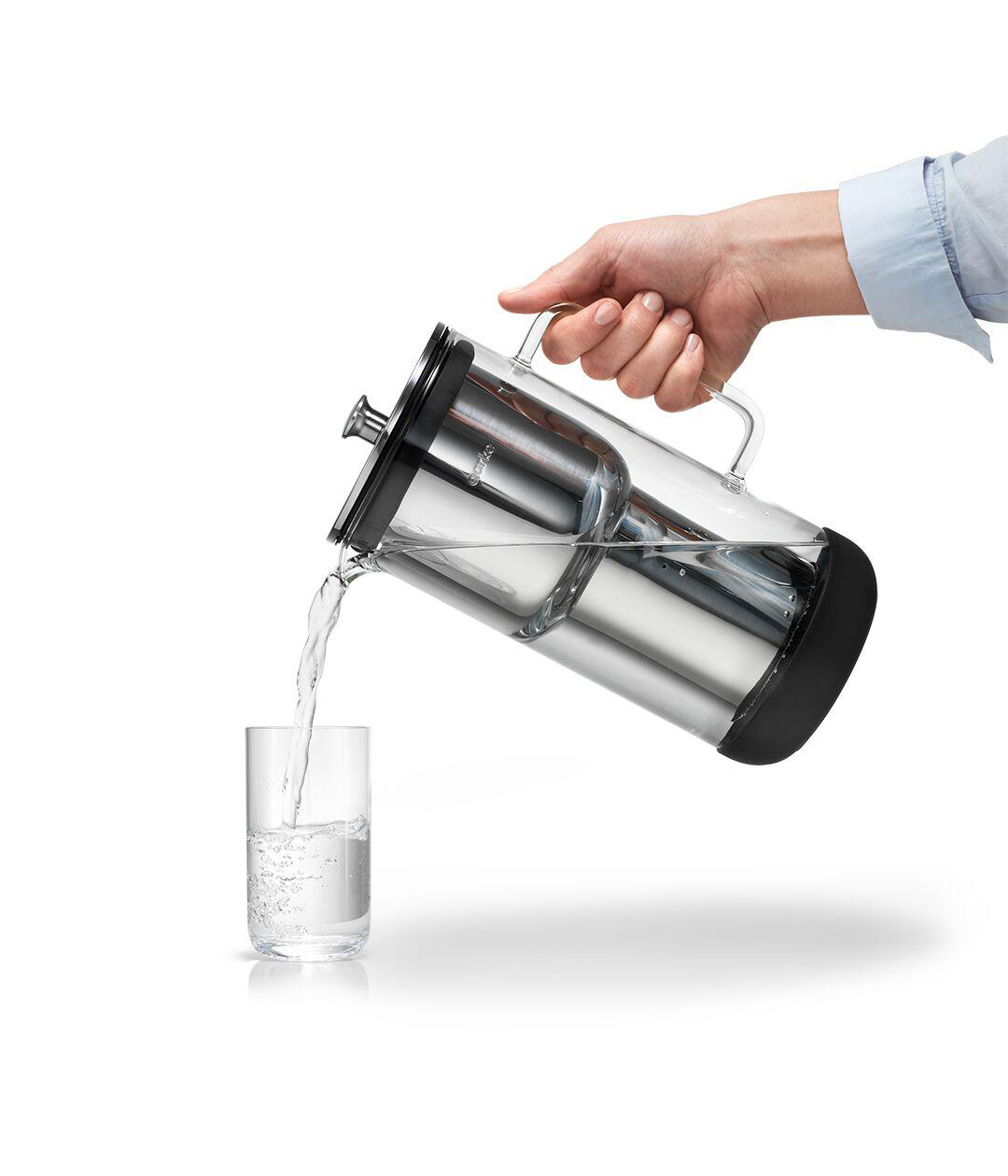 Eine Person gießt Wasser aus einem Glaskrug in ein Glas. Weißer Hintergrund.