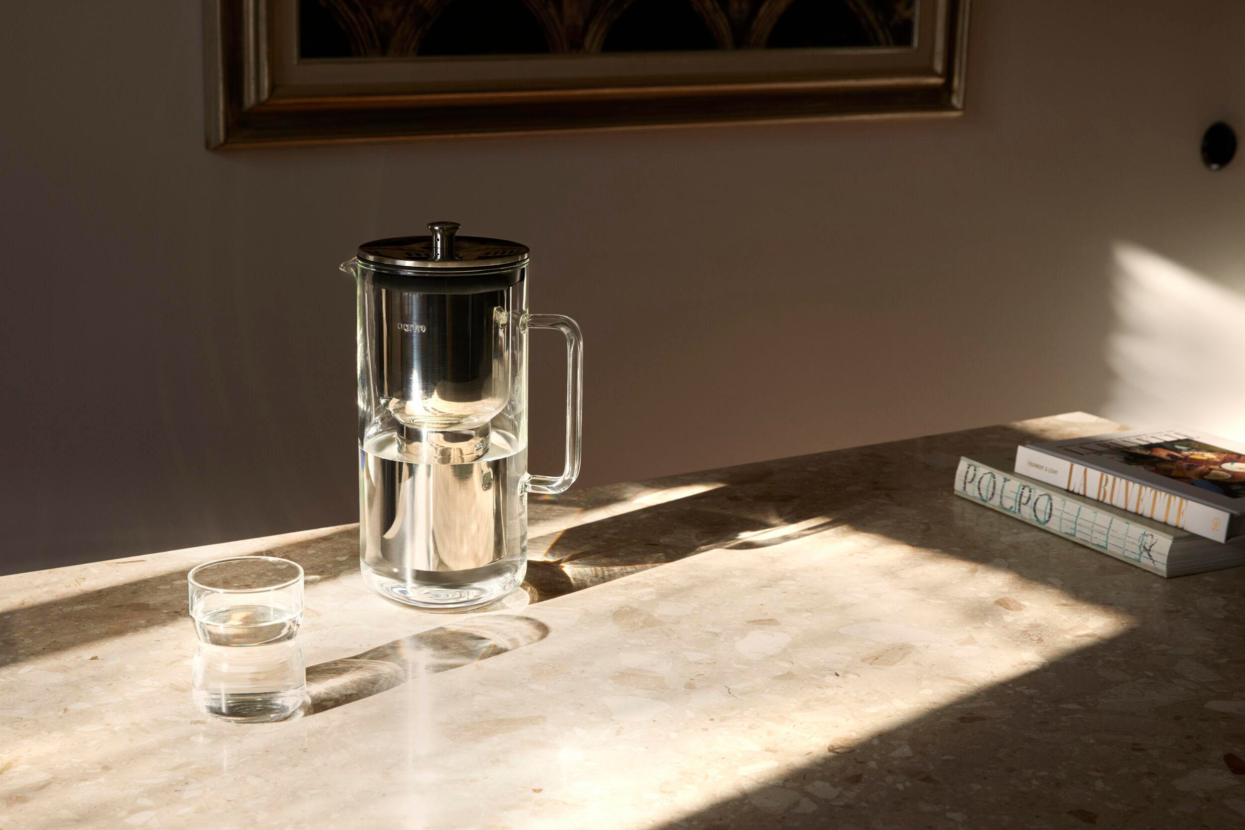 Glaskrug mit Filter, Glas und Bücher auf Marmortisch. Sonnenlicht.