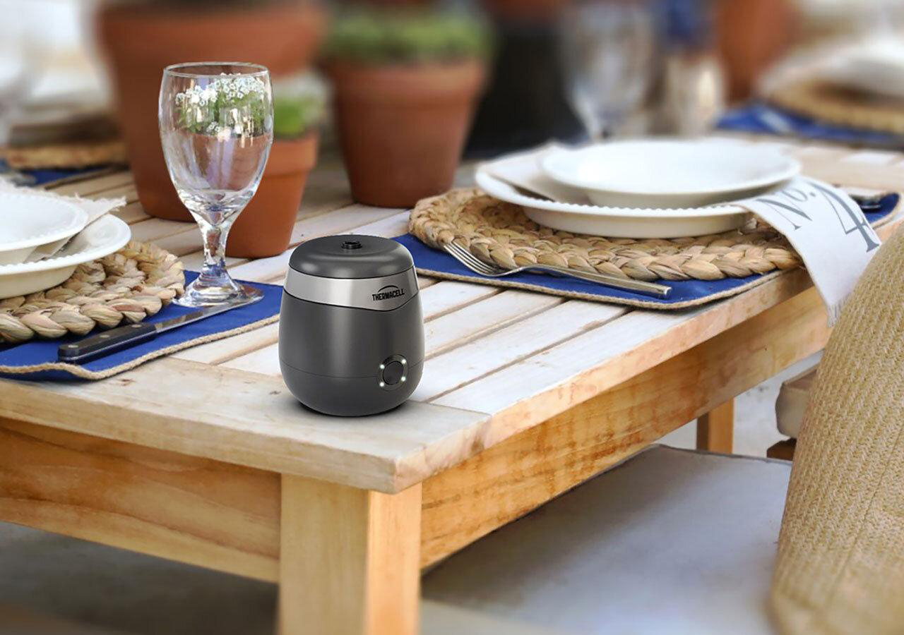 Ein schwarzes Thermacell-Gerät steht auf einem Holztisch, der zum Essen gedeckt ist.