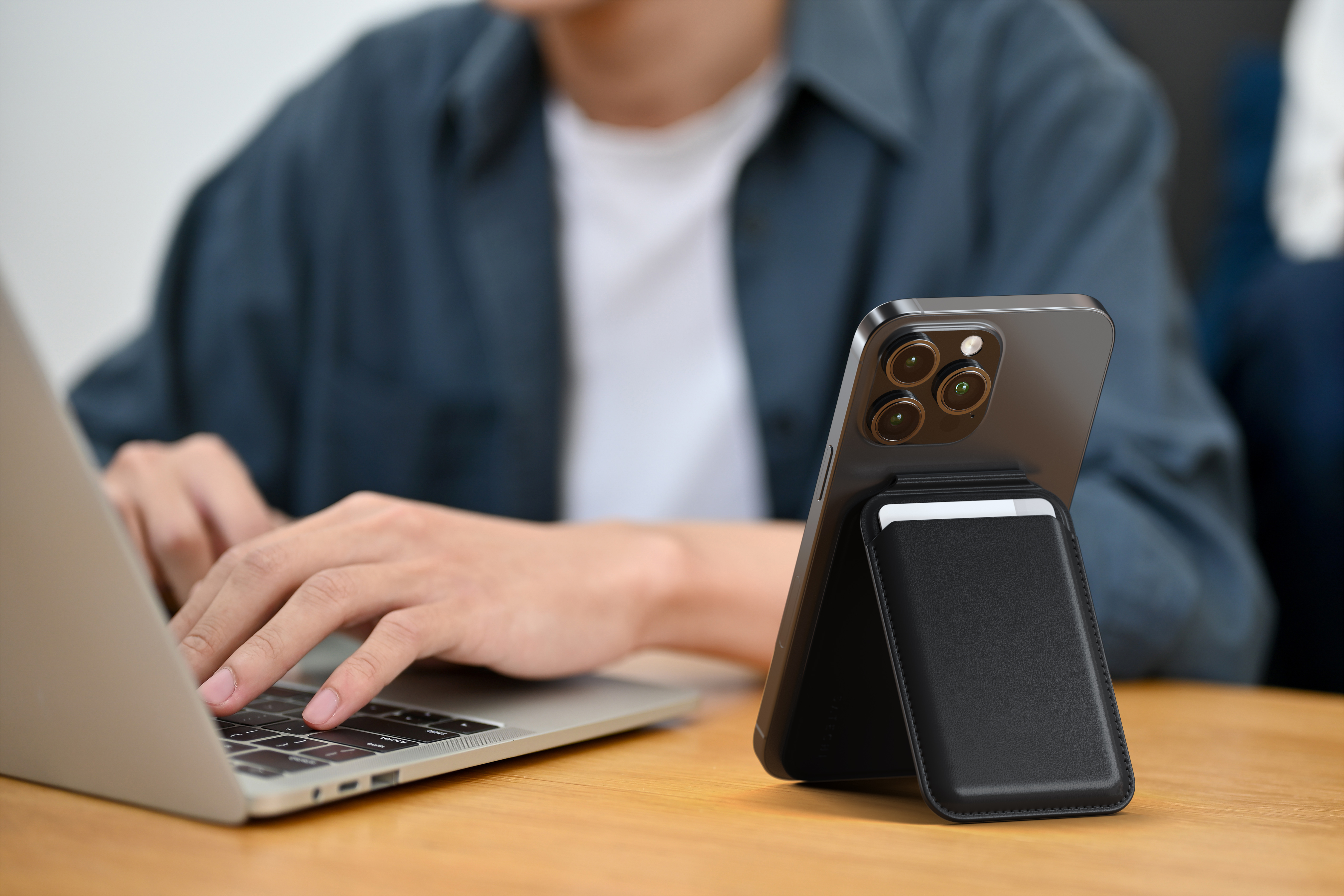 Egy személy laptopot használ, miközben egy kártyatartós telefon egy faasztalon áll.