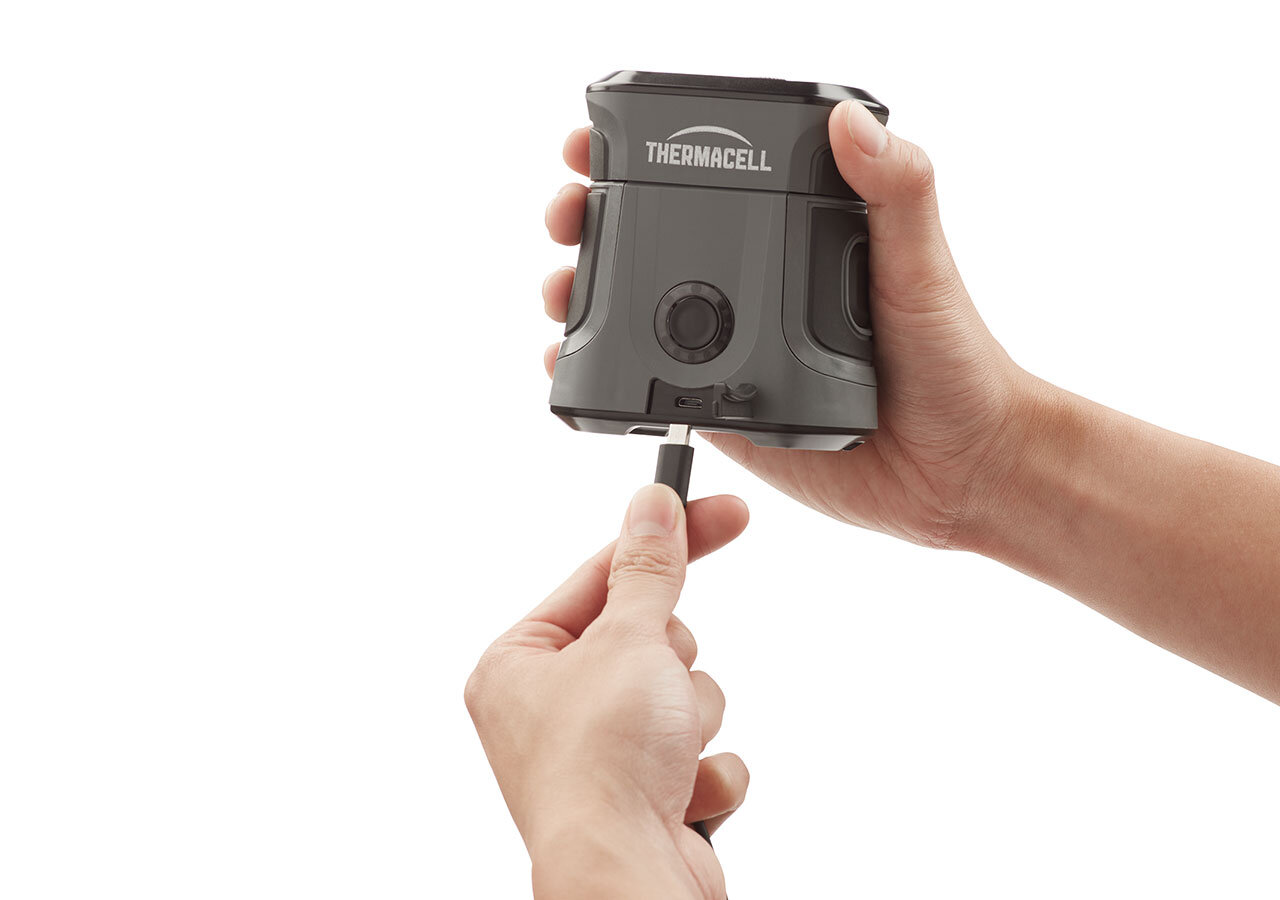 Hände stecken ein USB-Ladekabel in ein schwarz-graues Thermacell-Gerät.